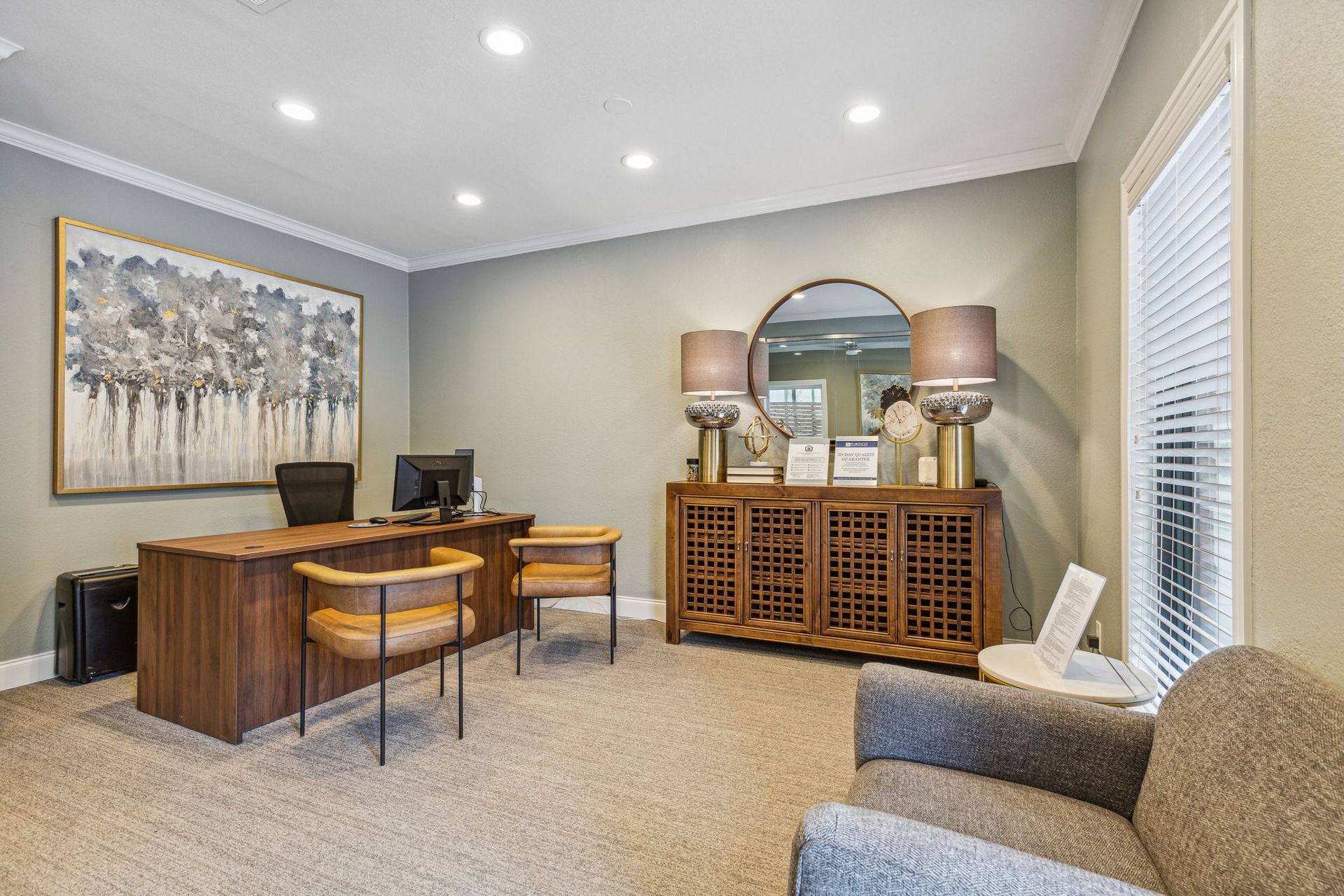 Office interior with desk, chairs, artwork, sofa, and decorative cabinet.