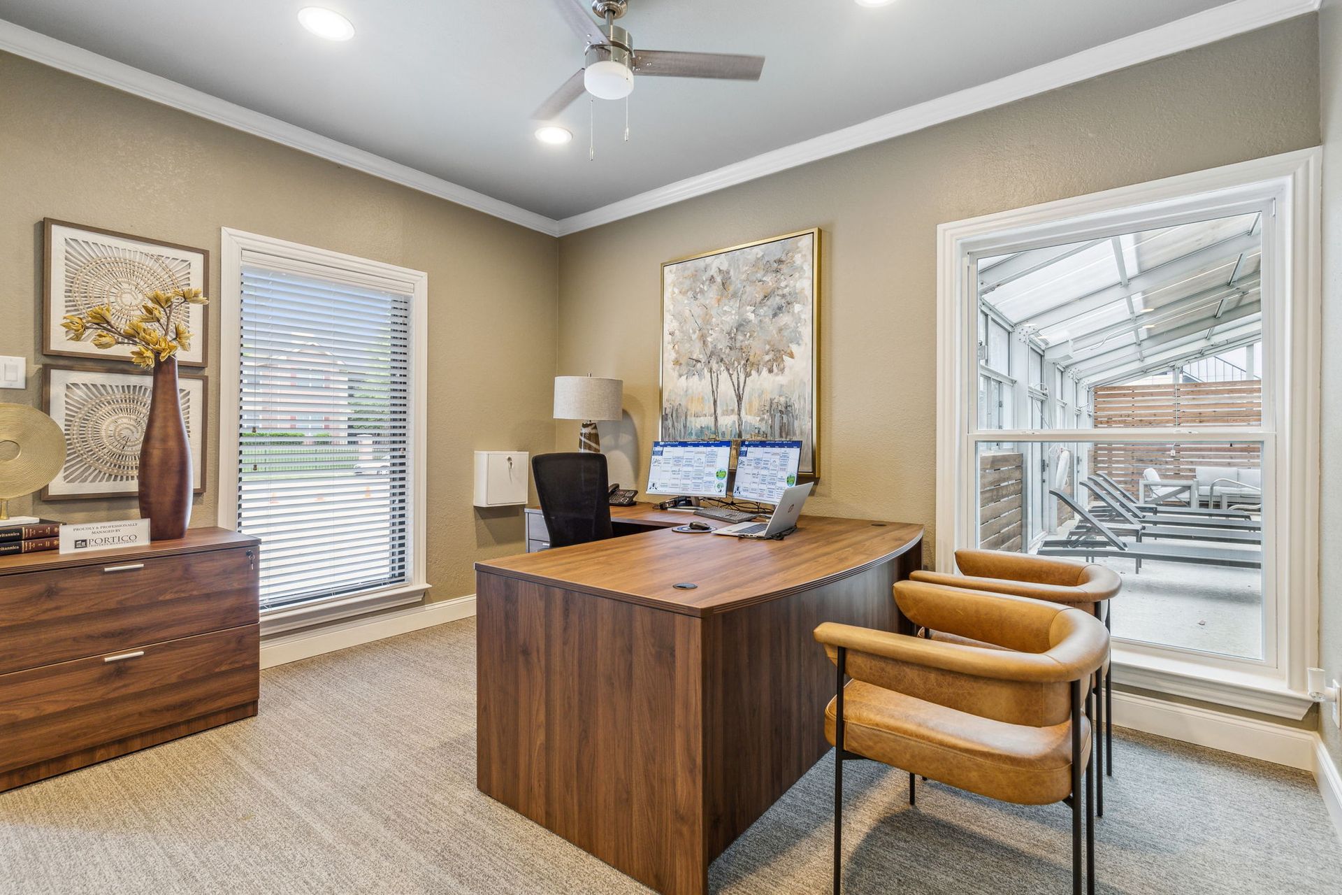 Office with wooden desk, two monitors, and two chairs near a window.