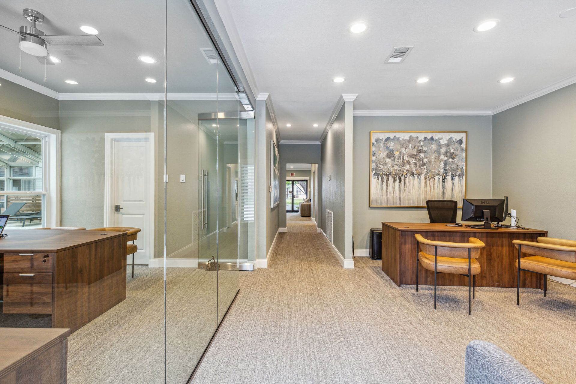 Office interior with wood desks, chairs, glass wall, long hallway, and art.