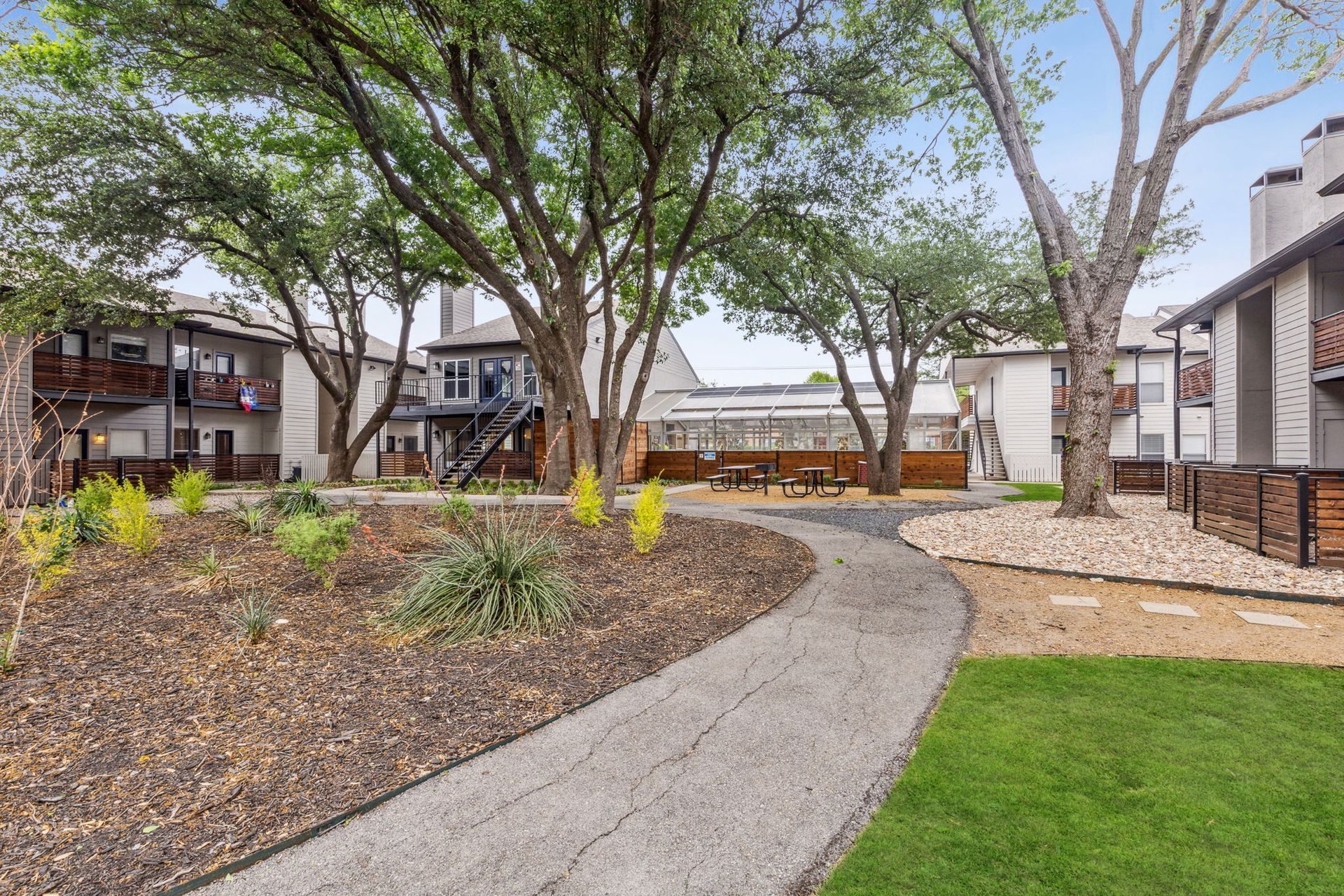 Stone path winds through apartment complex courtyard, leading to seating area, shaded by trees.