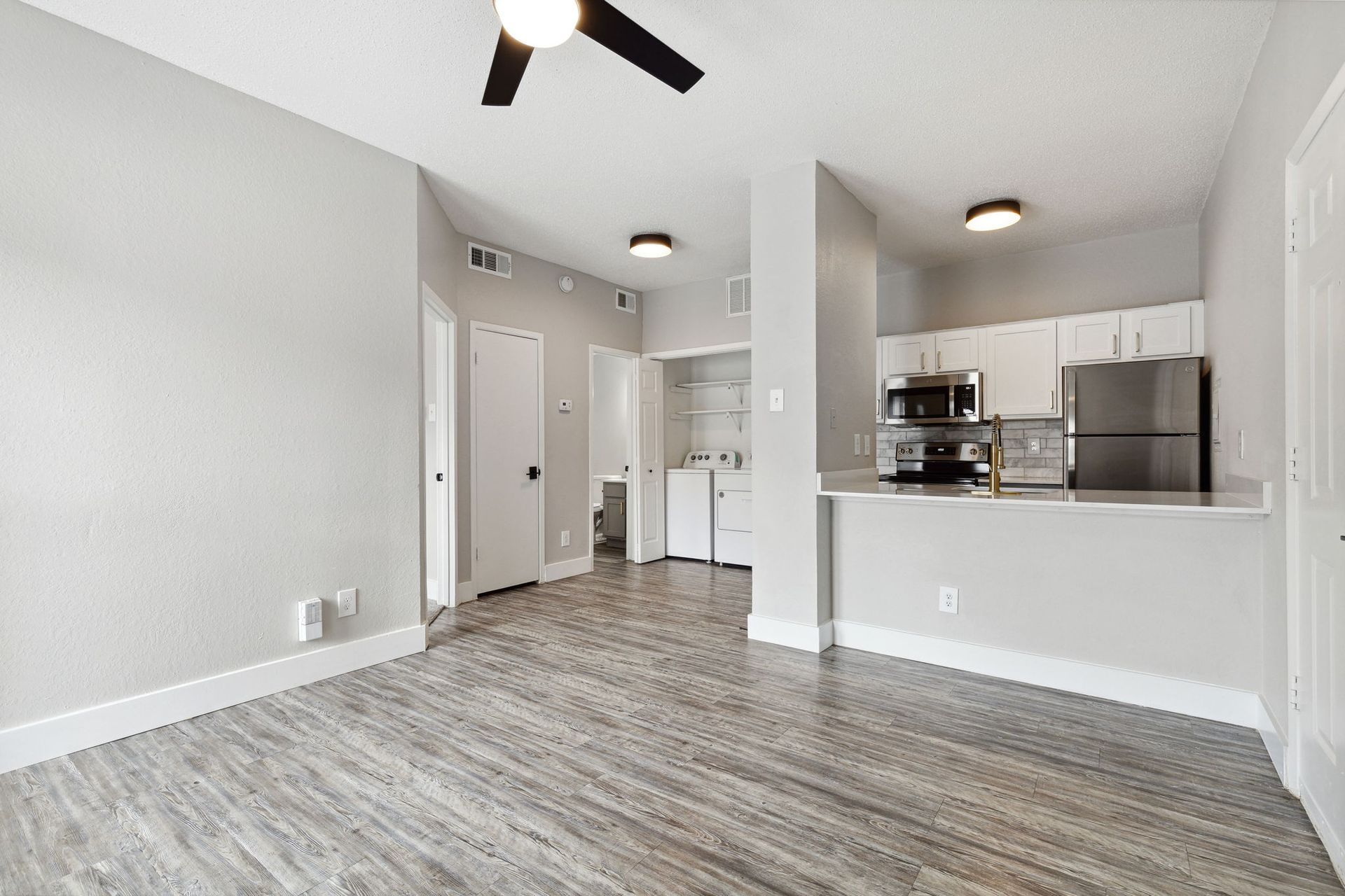 Grey-walled living space with a kitchen and a ceiling fan; grey wood-look flooring.