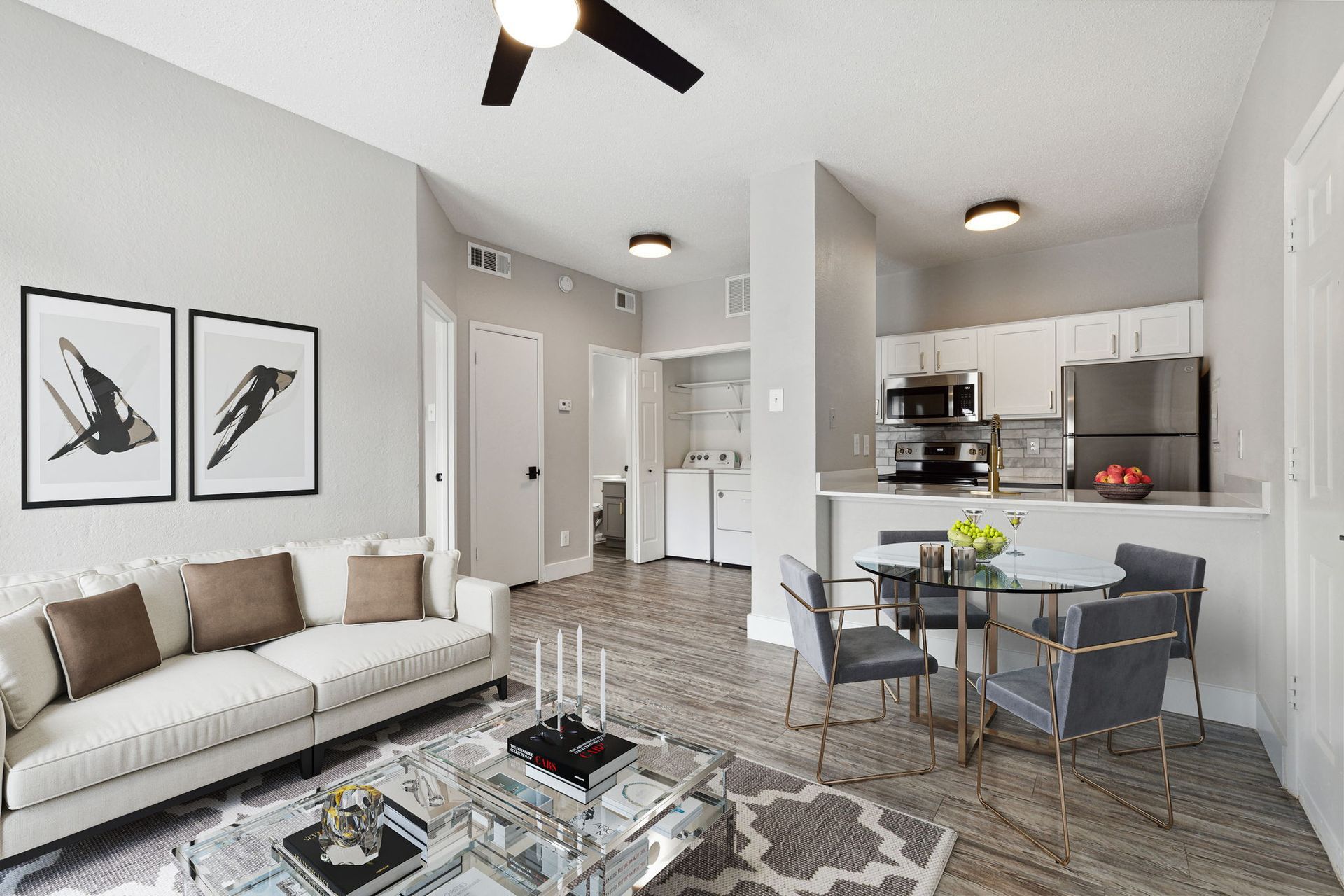 Living room and kitchen combo with white sofa, glass dining table, and stainless steel appliances.