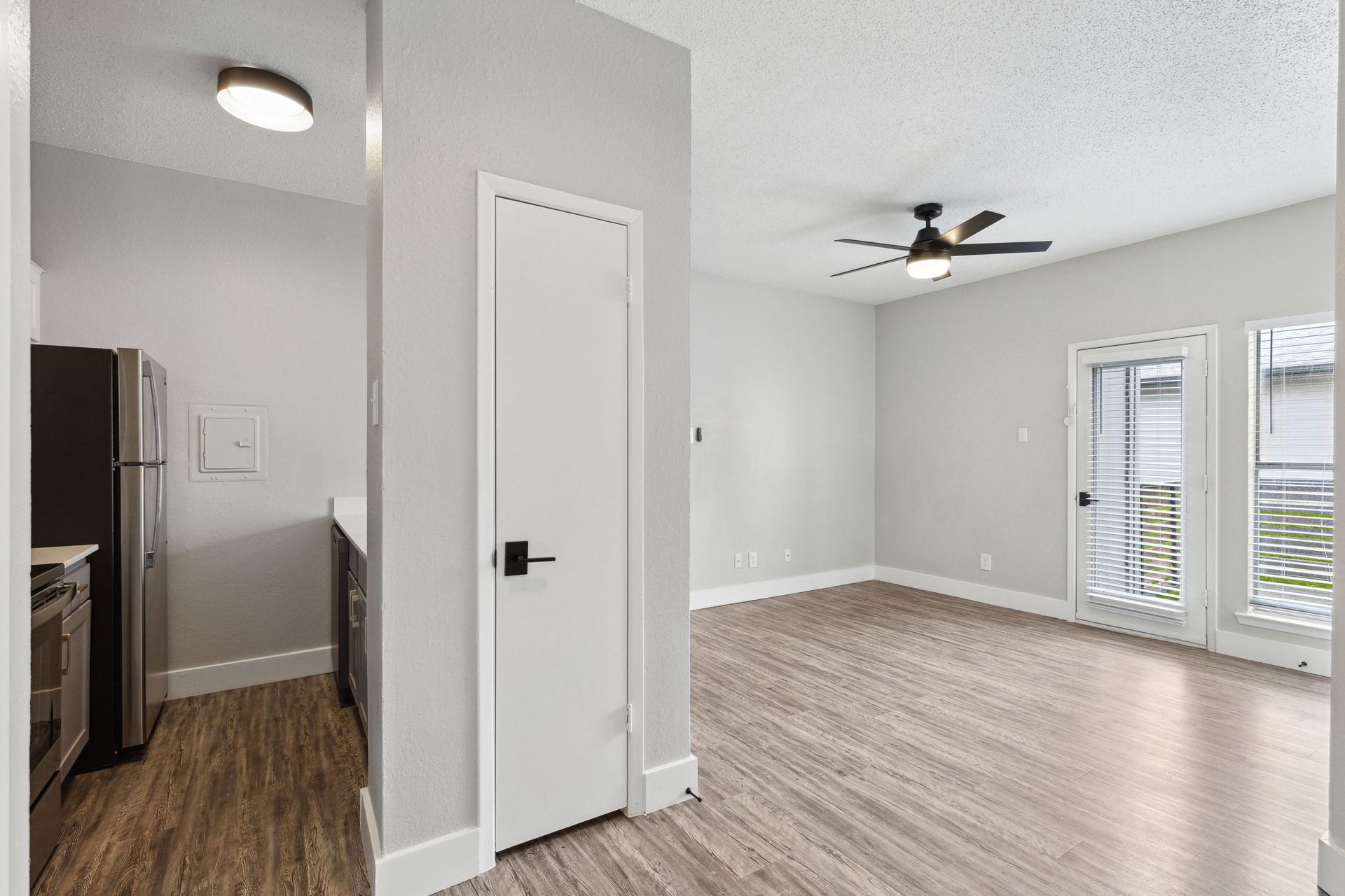 An empty apartment interior with light gray walls, wooden floors, and a dark ceiling fan.