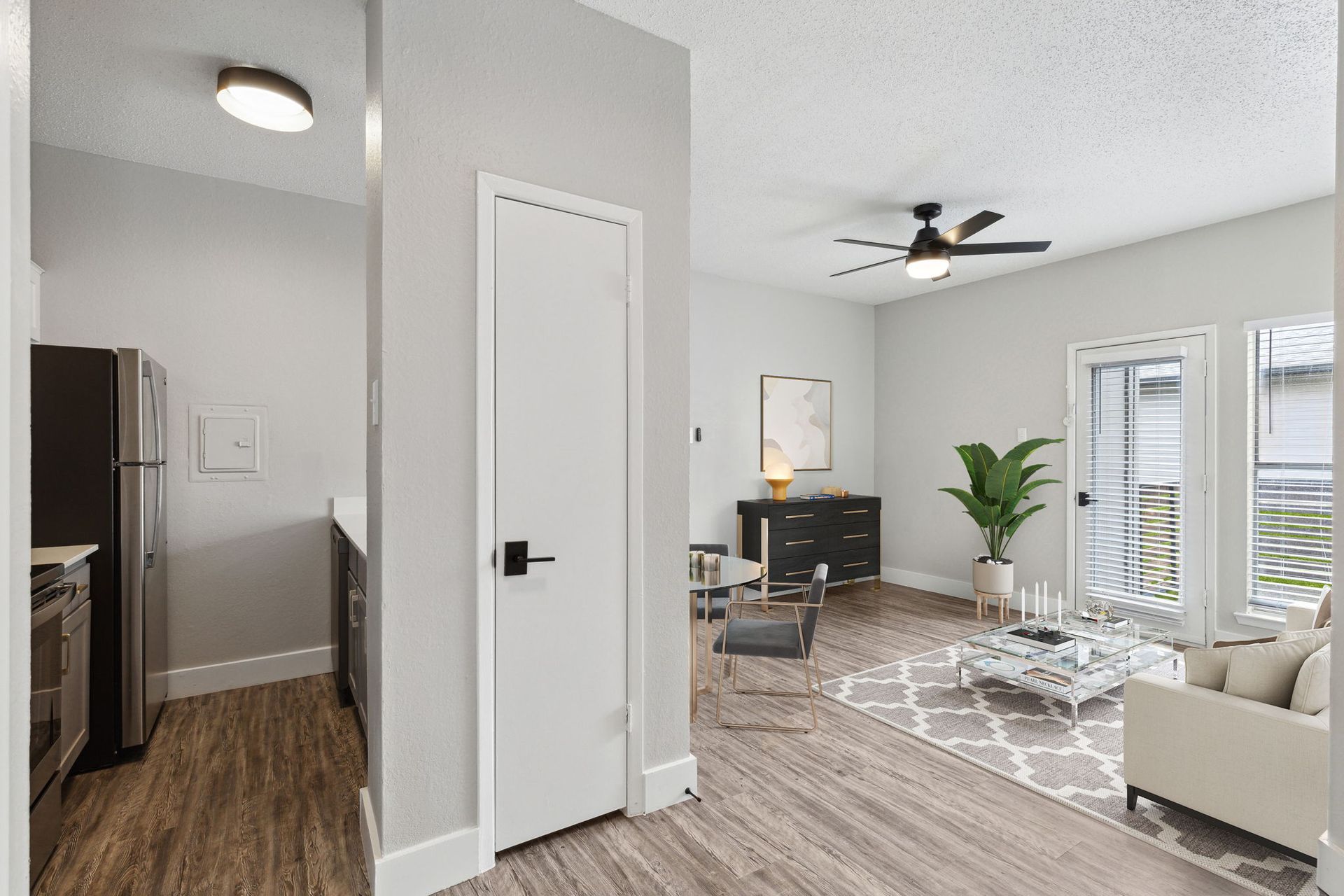 Interior view of an apartment with light walls, wood-look flooring, and access to a kitchen, living room, and balcony.