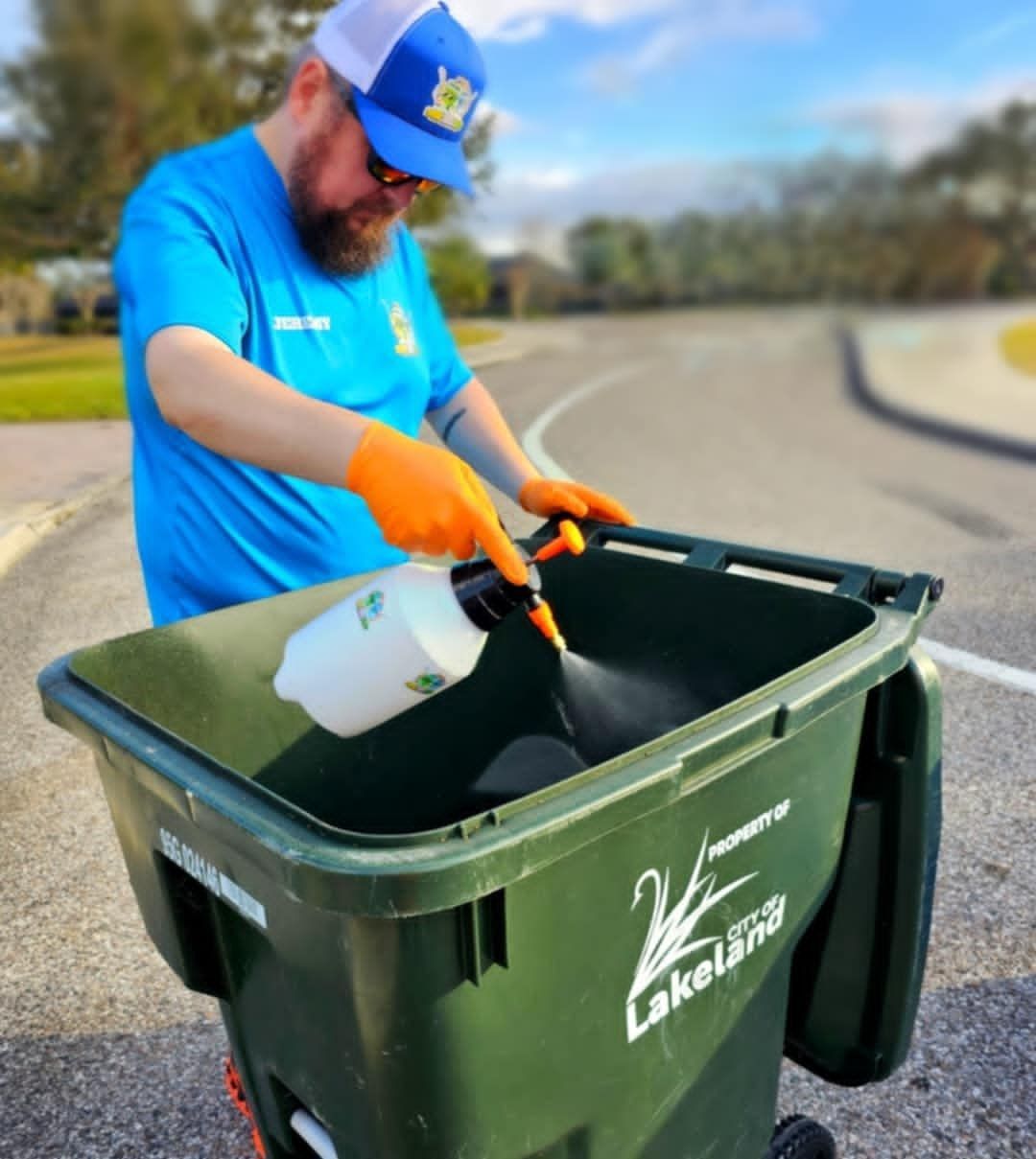 A man is spraying a green trash can with a spray bottle.