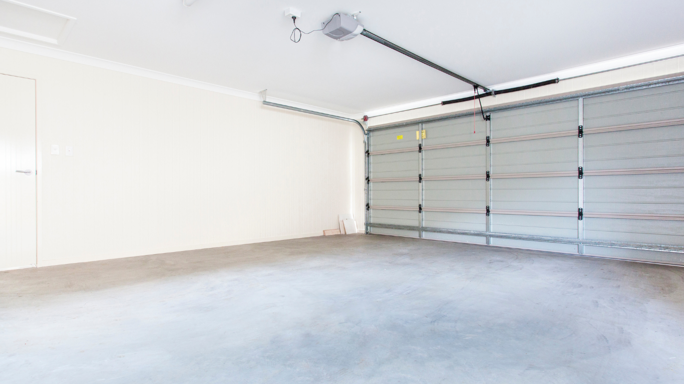 Empty white garage interior with closed gray sectional door and concrete floor
