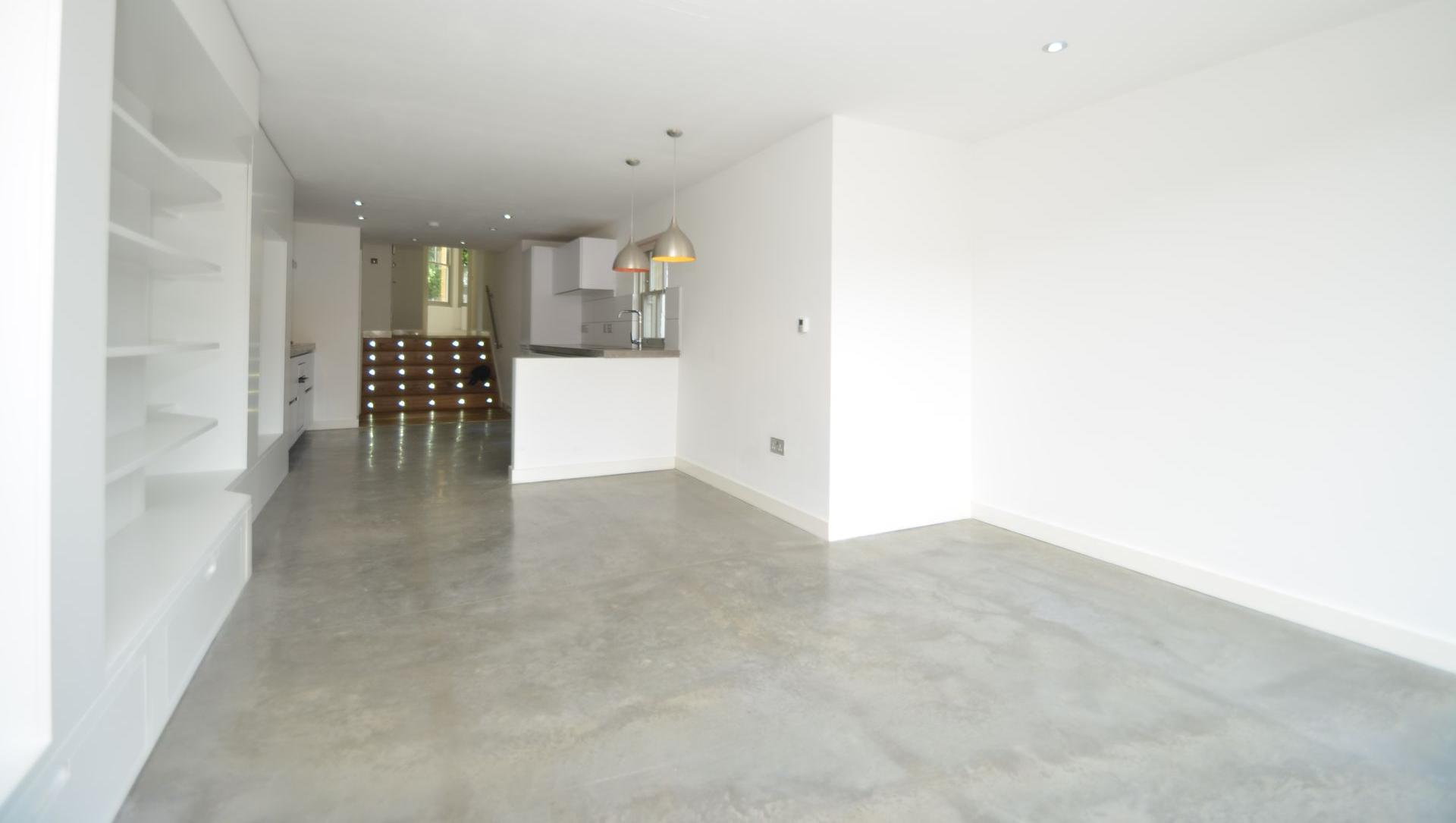 Empty white living room with gray floor and open kitchen area