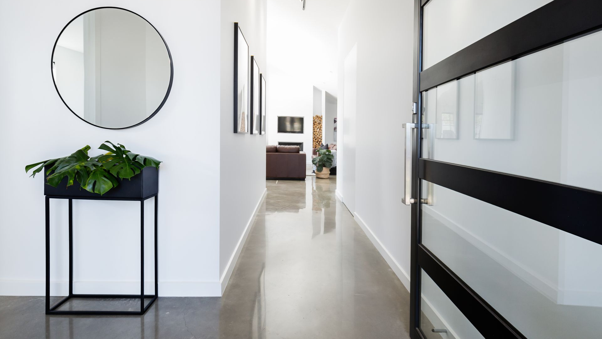 Bright hallway with white walls, a round mirror, black planter, and glass doors.