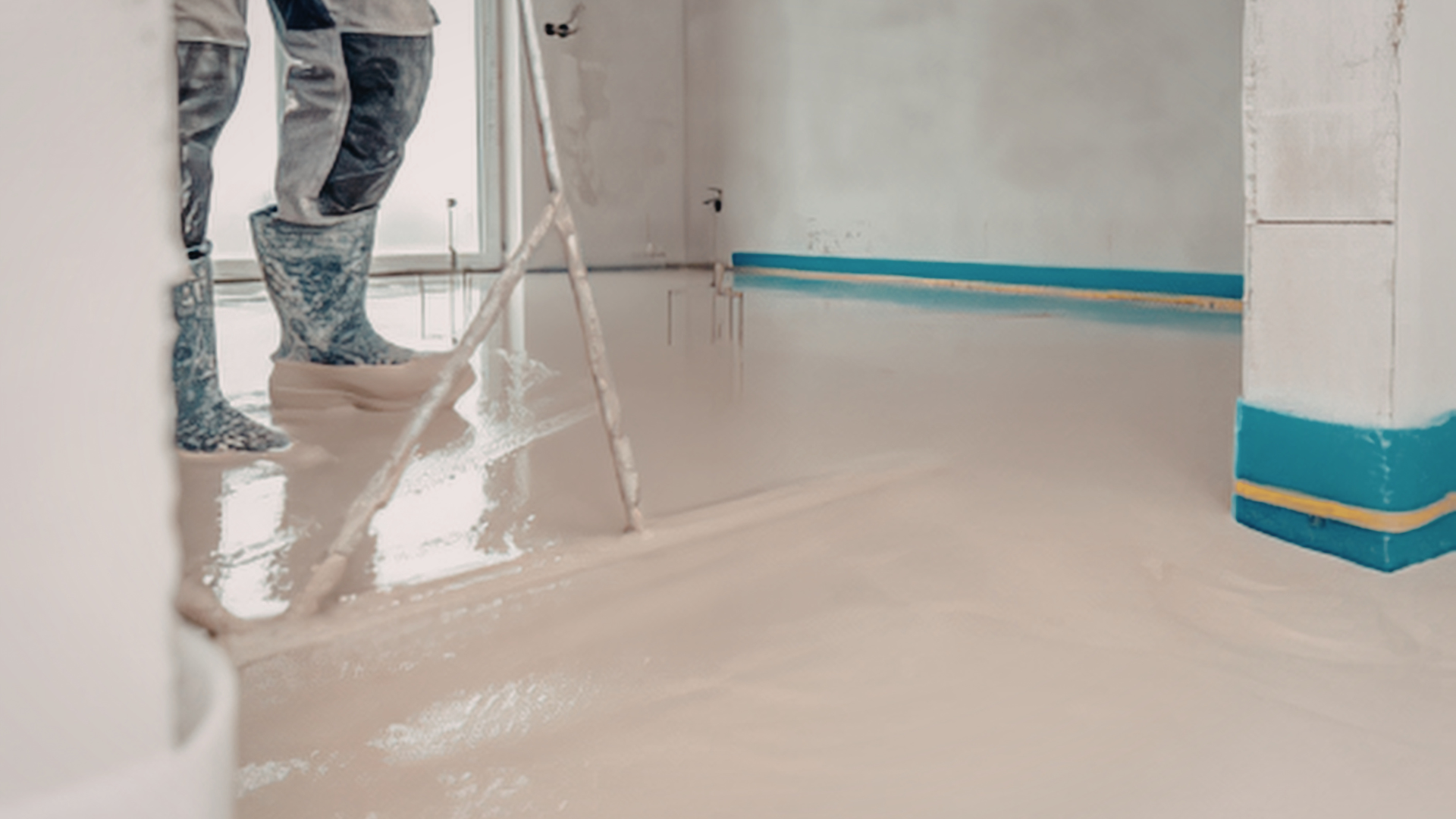 Construction workers in protective boots level fresh, light-colored self-leveling compound on a room floor.