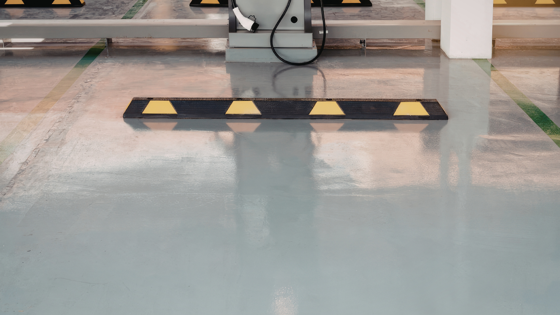 A black and yellow speed bump sits on a smooth, grey epoxy floor in an industrial charging or parking area.