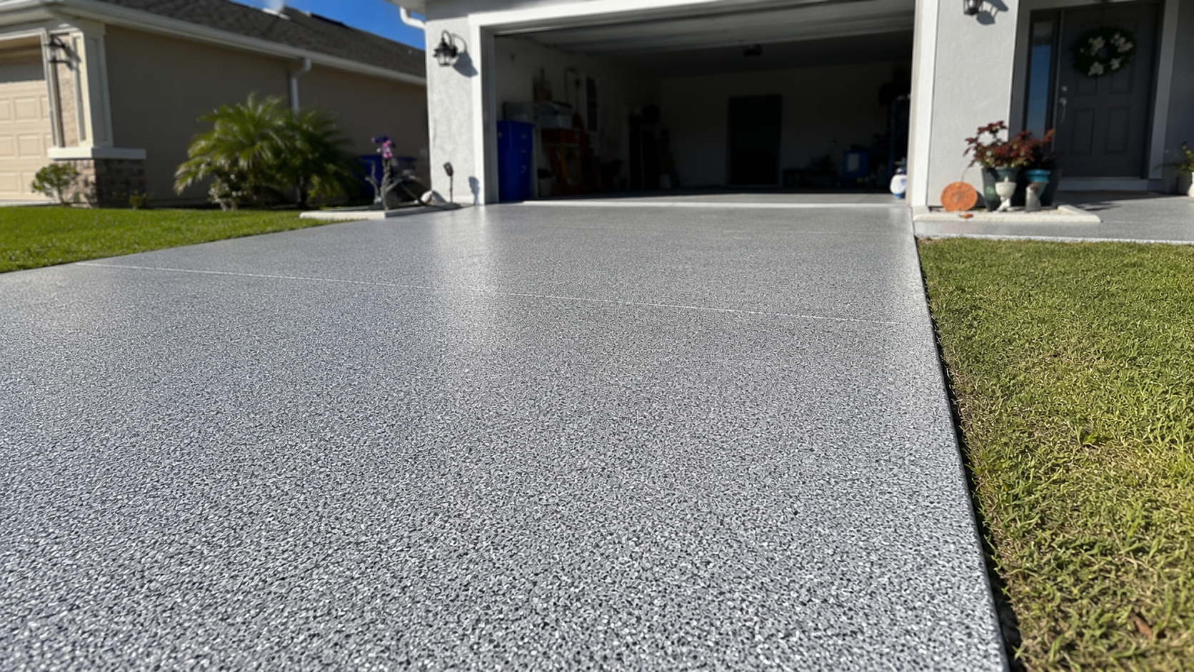 Speckled gray epoxy driveway leading to an open garage beside a green lawn and house exterior.