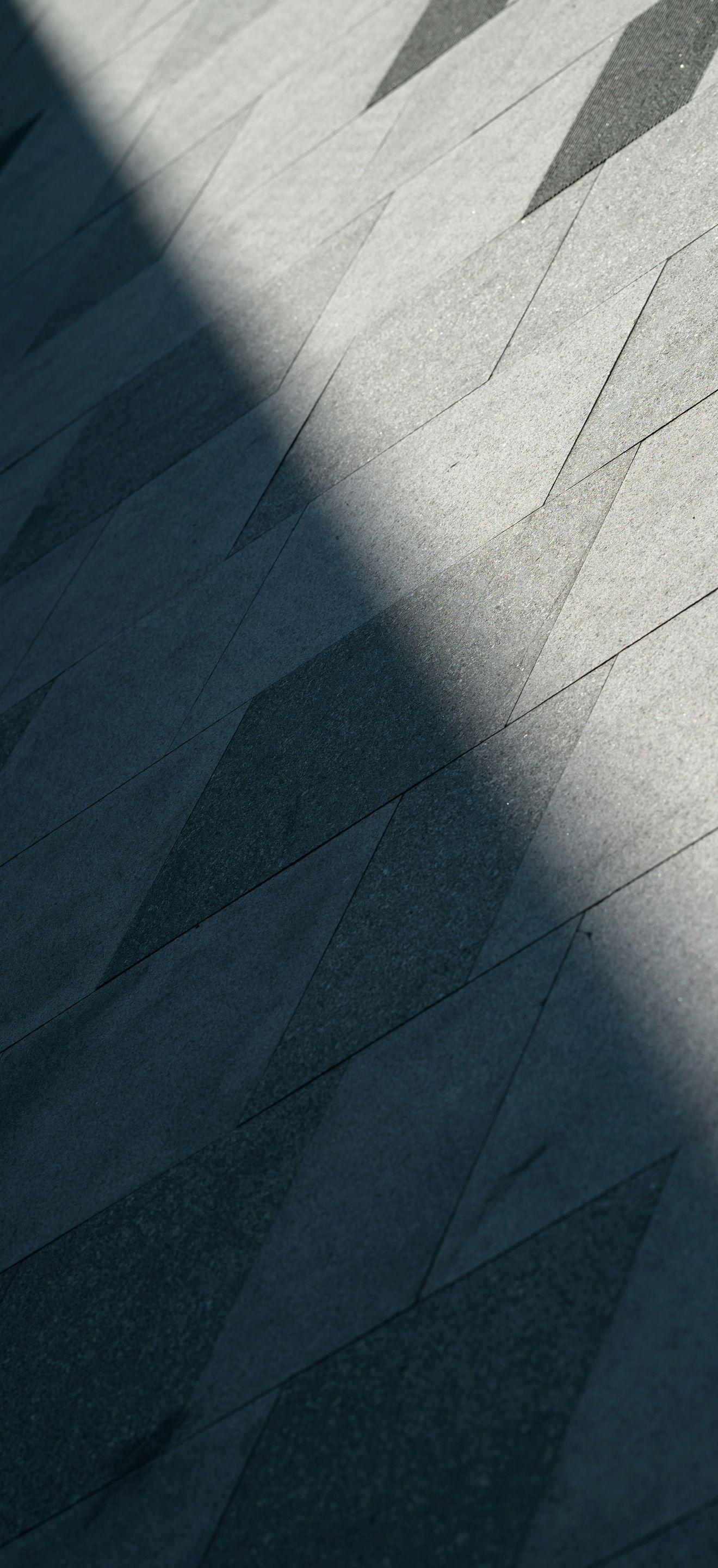 Diagonal shadows across a light gray textured surface with a small dark grid pattern in the corner