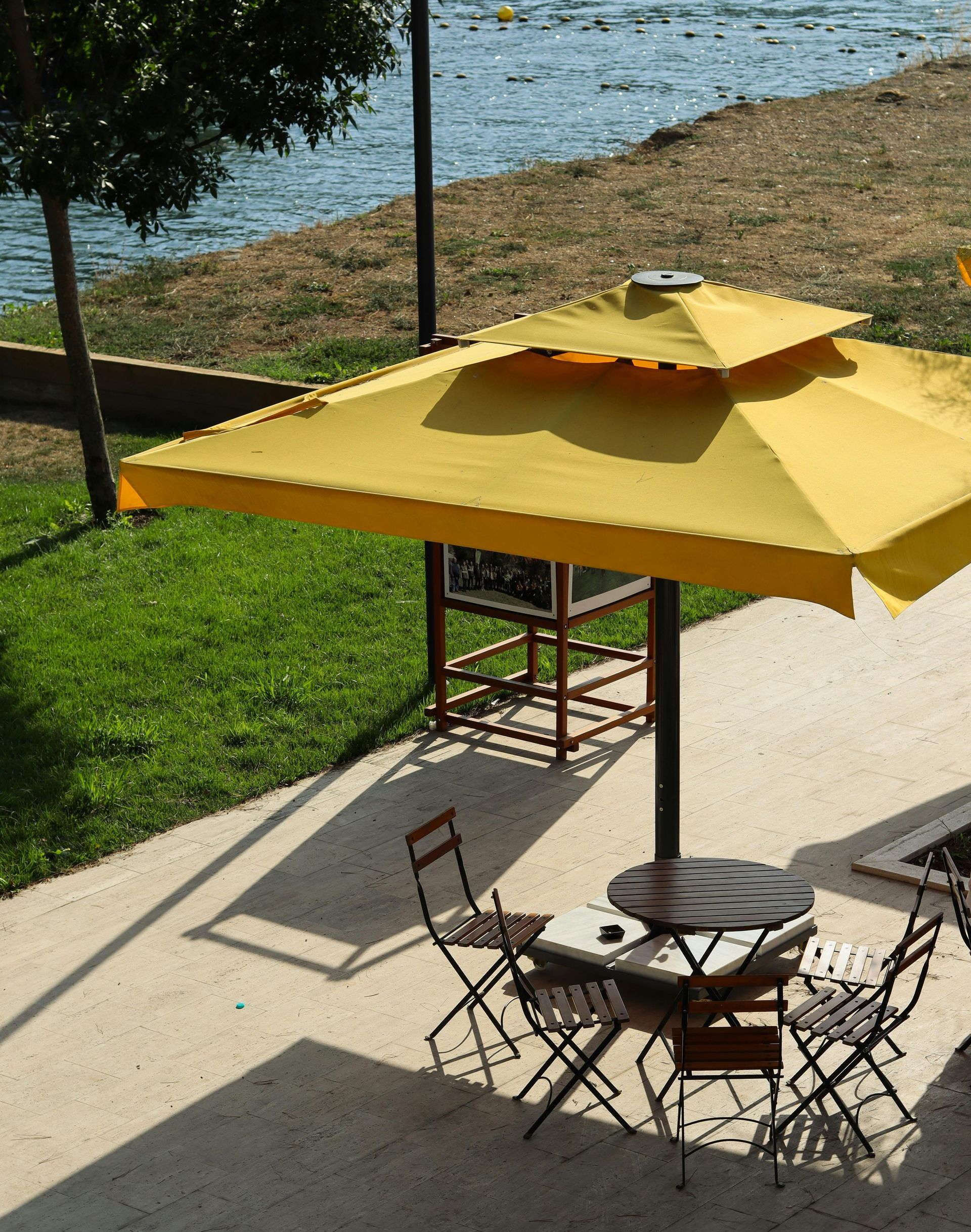 Patio table and chairs under a yellow umbrella beside a waterfront lawn and walkway