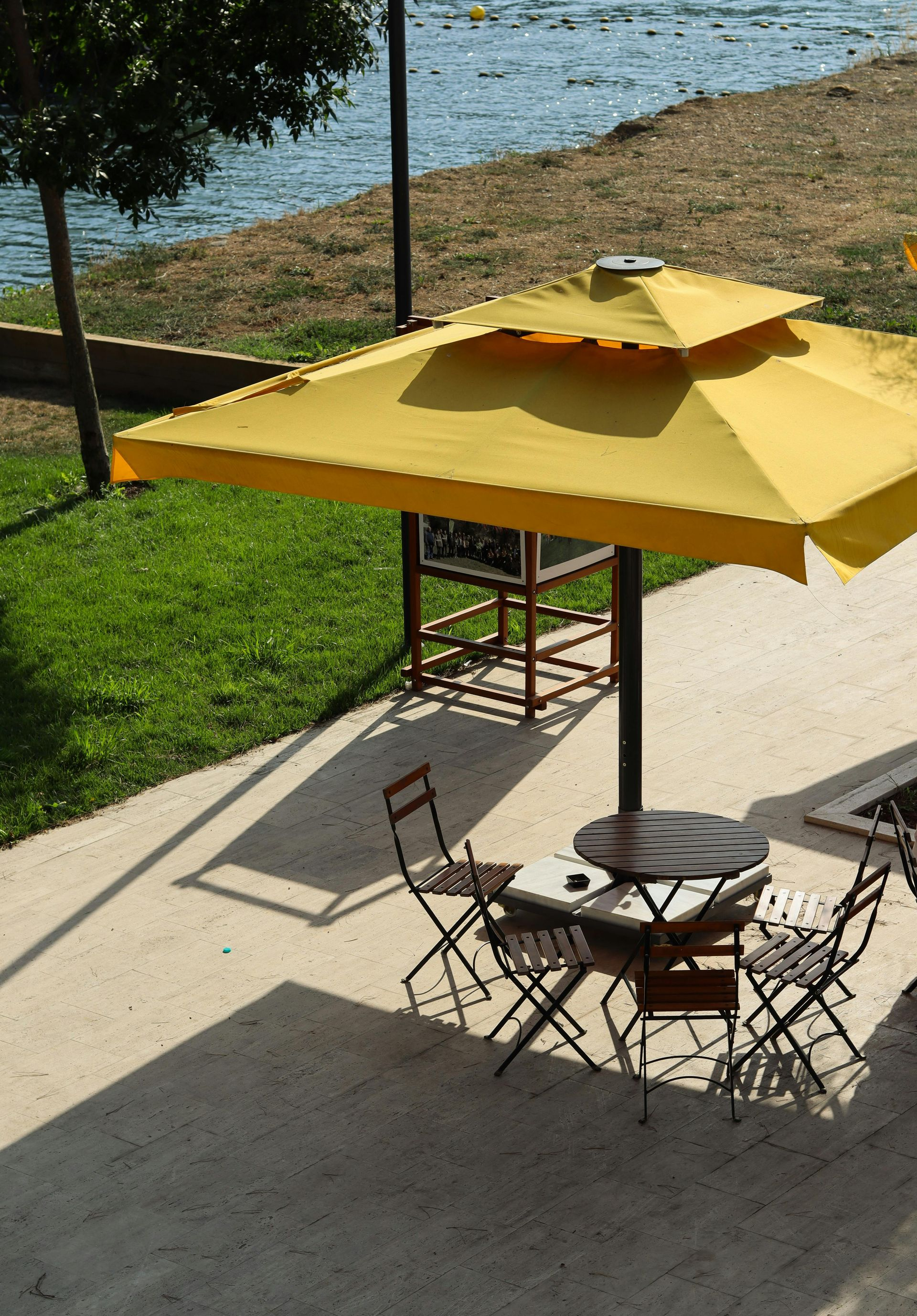 Outdoor patio with yellow umbrella, round table, and folding chairs beside the water