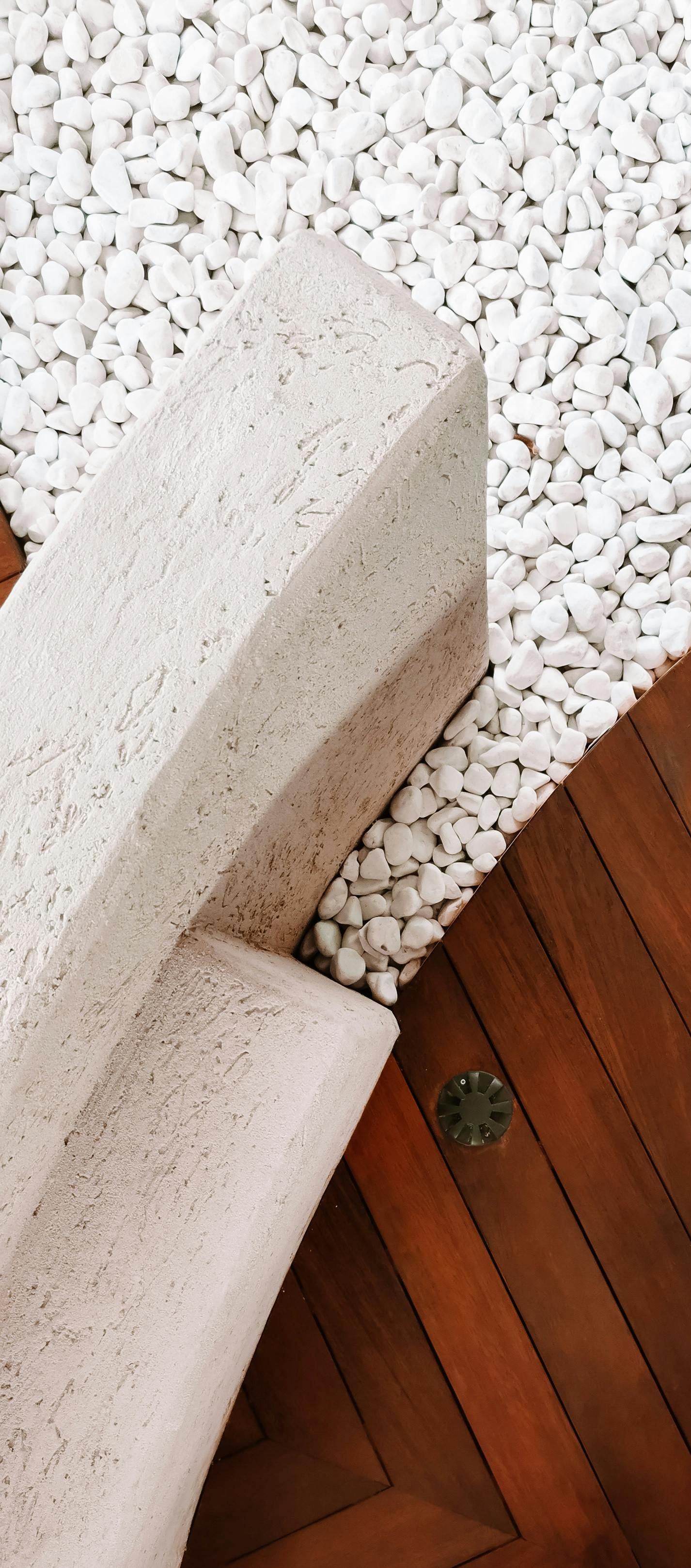 White pebbles beside a wooden deck and a light-colored concrete bench corner