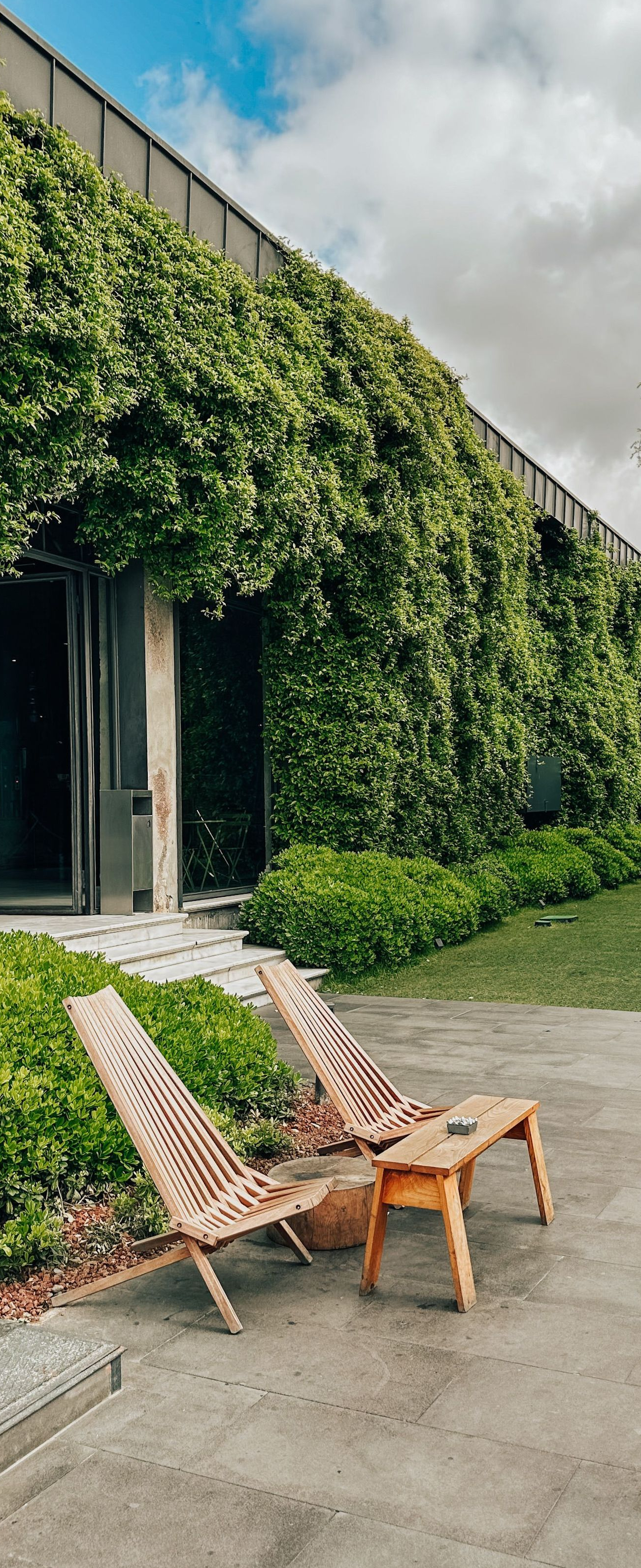 Vine-covered modern building with open doors and two woven lounge chairs on a paved patio