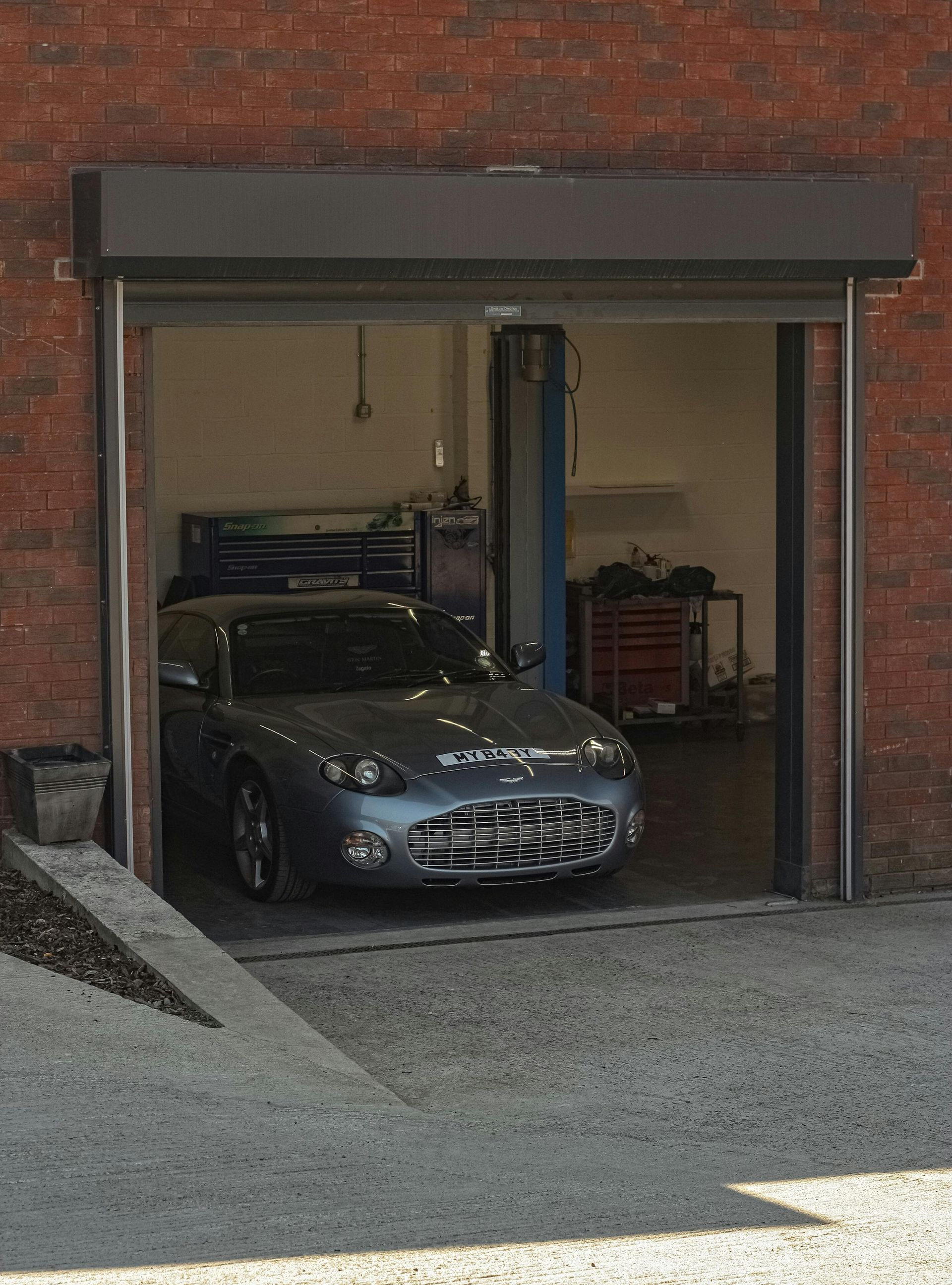 Silver sports car parked in a partially open garage with a brick exterior.
