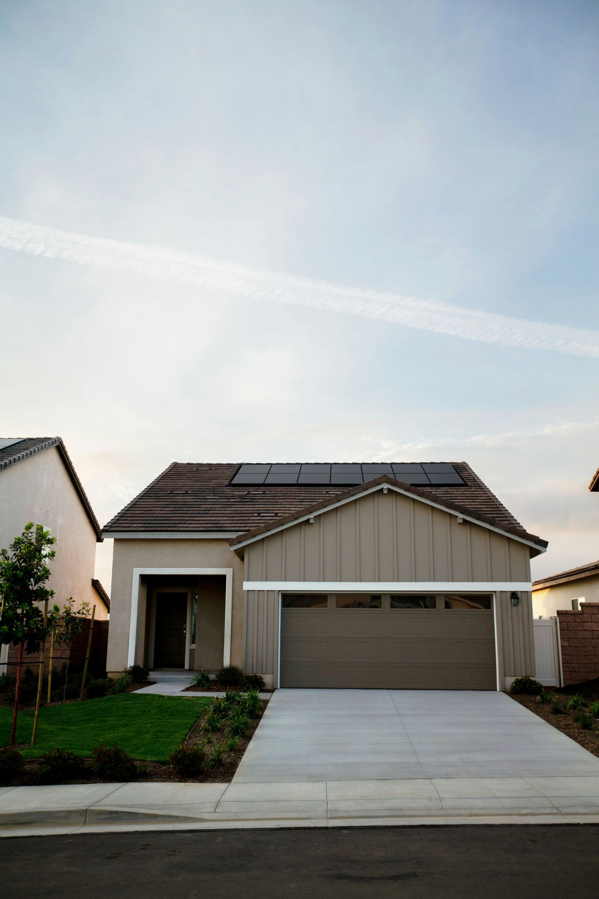 Suburban single-story house with a two-car garage, driveway, and a clear sky overhead.