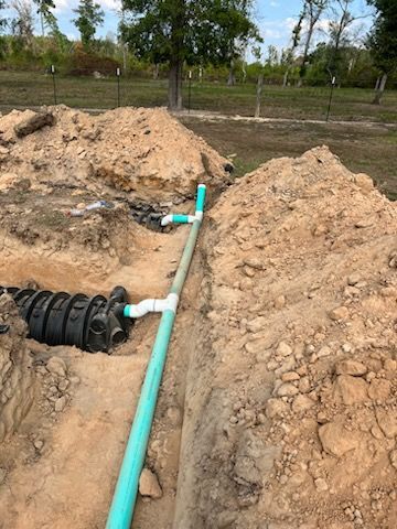 A green pipe is laying in the dirt next to a pile of dirt.