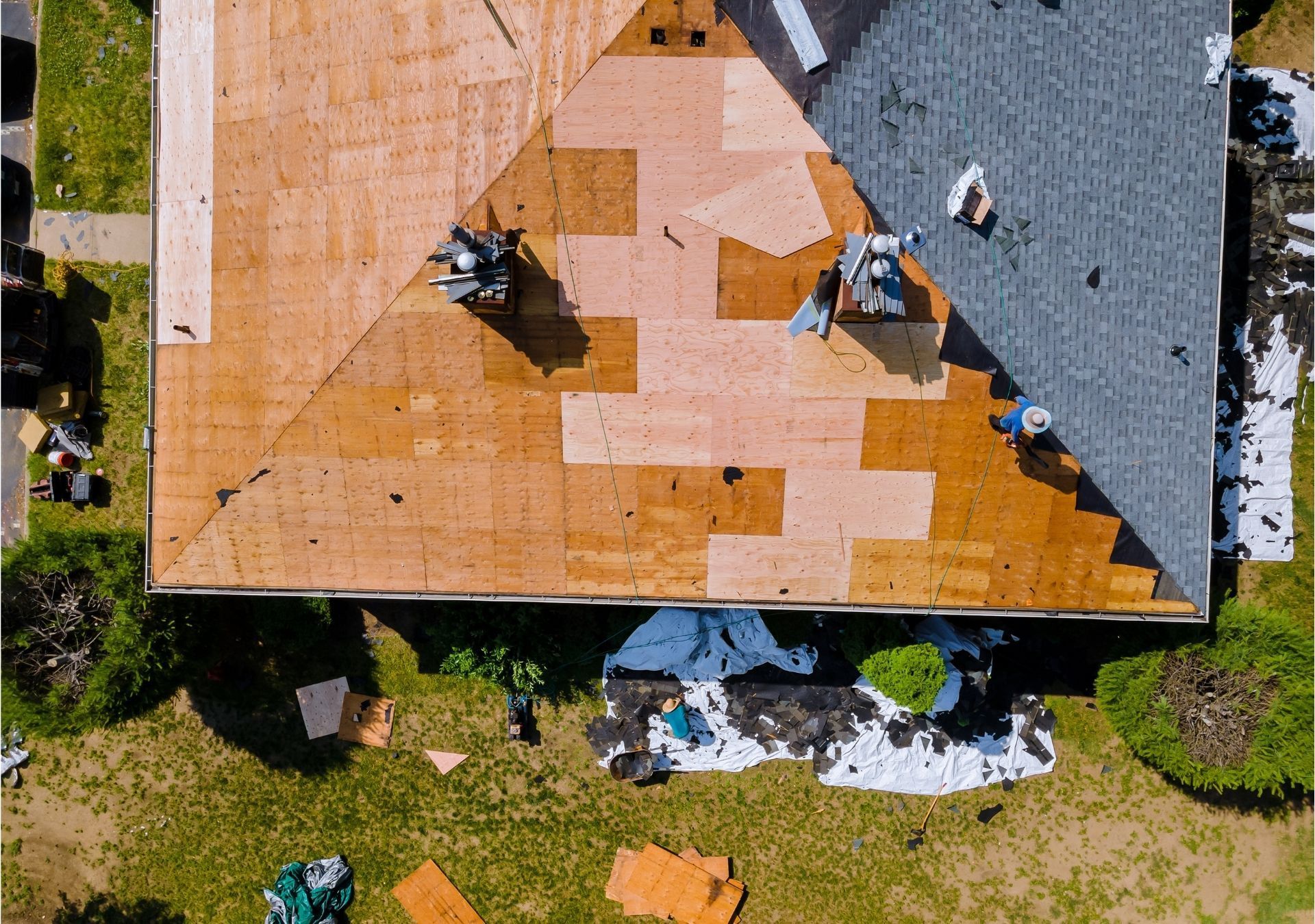 Overhead view of a house roof partially replaced. Brown exposed underlayment, gray shingles, and workers are visible.