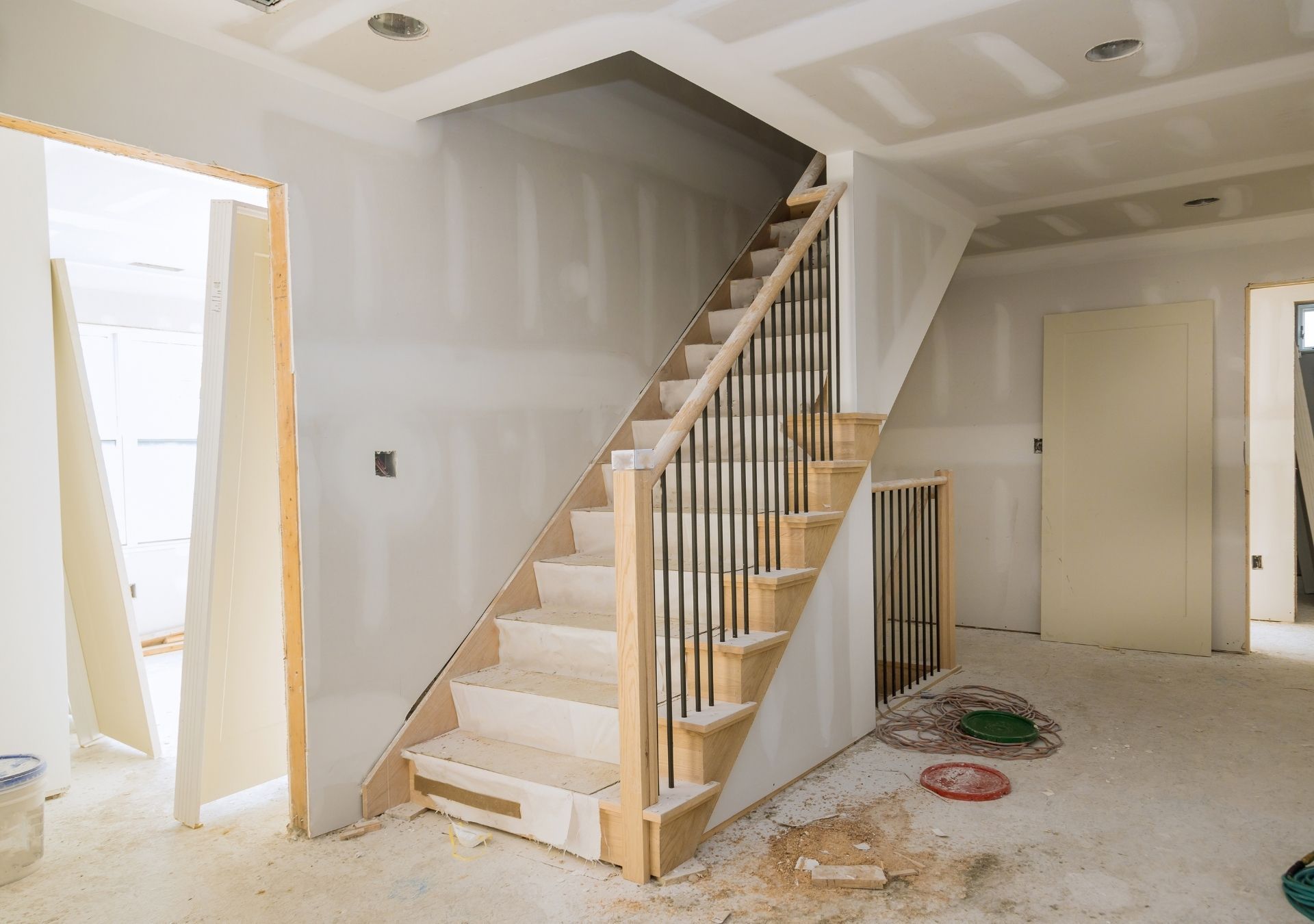 Interior view of a house under construction, staircase with wooden steps and black railings, drywall unfinished.