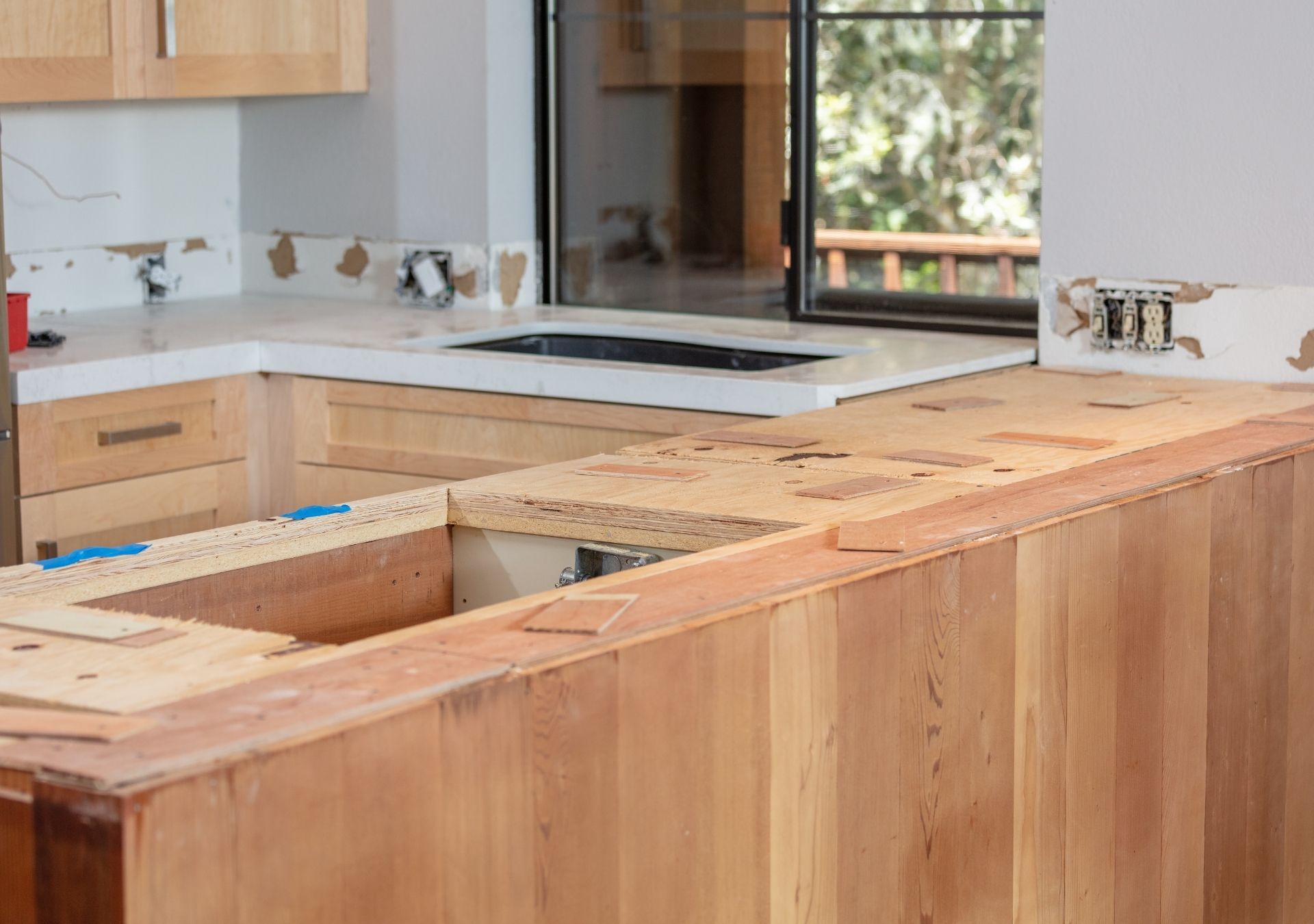 Kitchen under construction: wood cabinets, countertop, sink opening, window to outside.