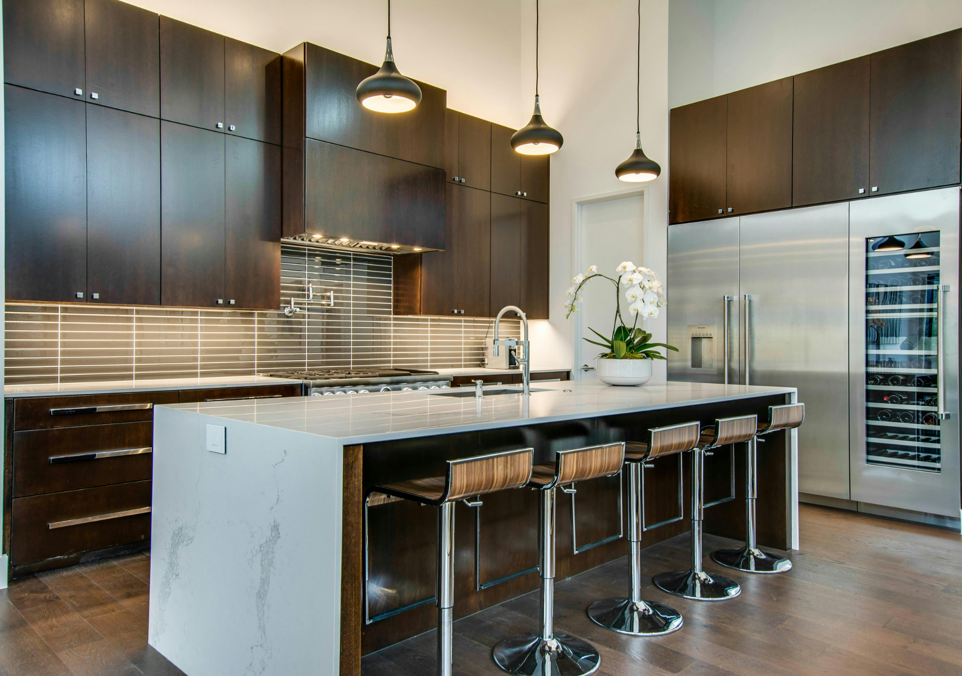 Modern kitchen with dark wood cabinets, large island with bar stools, and stainless steel appliances.