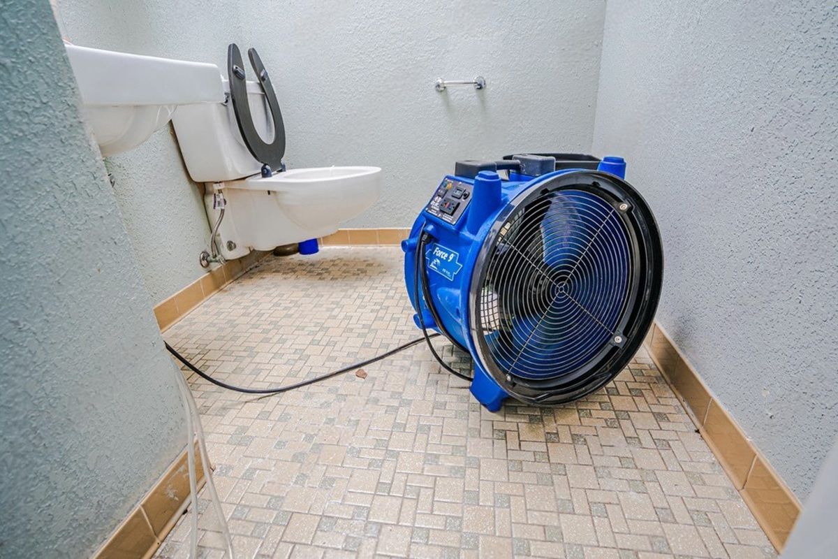 A large blue fan drying a bathroom floor next to a toilet.