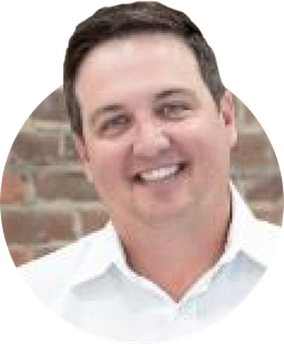 a man in a white shirt is smiling in front of a brick wall .