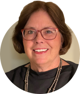 a woman wearing glasses and a pearl necklace smiles for the camera