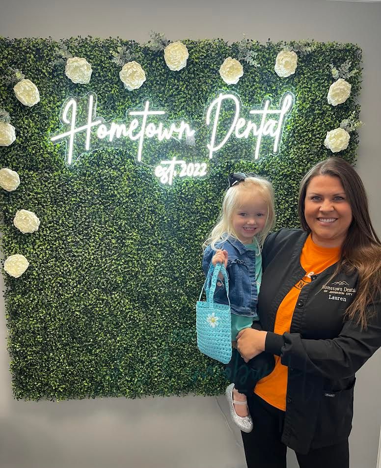 Woman in scrubs holds a smiling child in front of a wall with a 