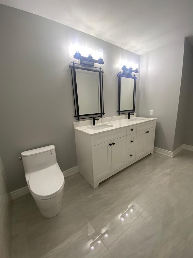 Bathroom with a white double vanity, two mirrors, a toilet, and gray walls.
