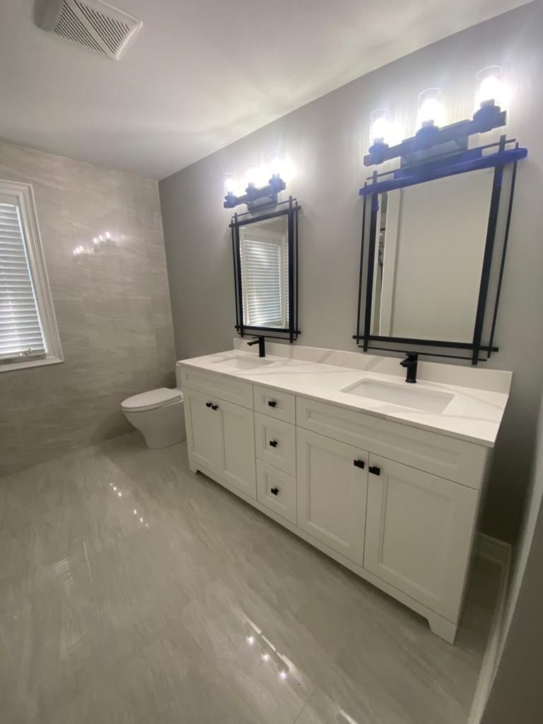 Modern bathroom with double vanity, mirrors, and lighting fixtures. White cabinets, gray walls, and tile flooring.