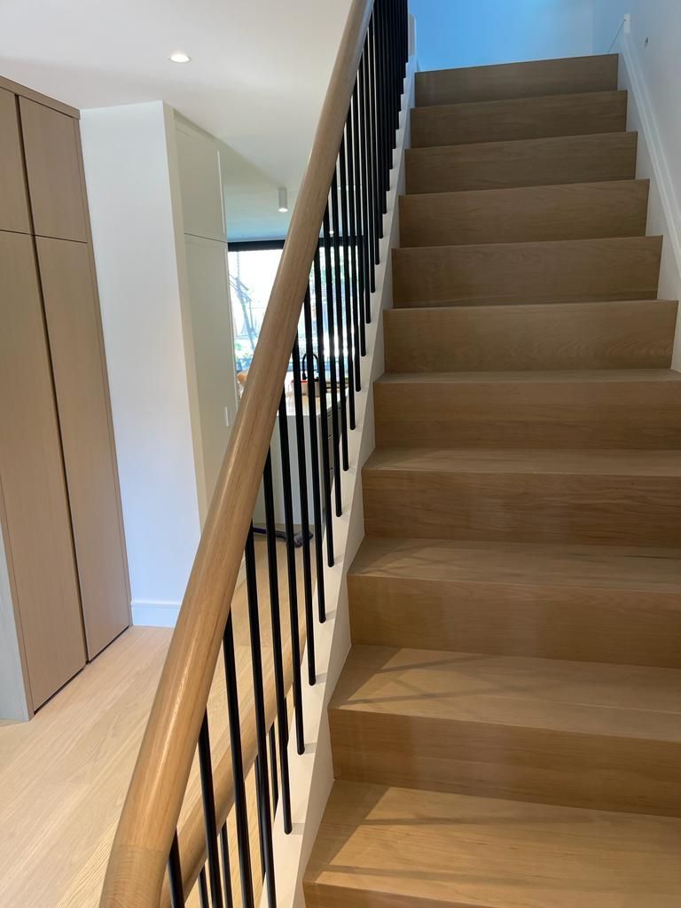 Wooden staircase with black metal balusters and a light-colored wood handrail, leading upwards.