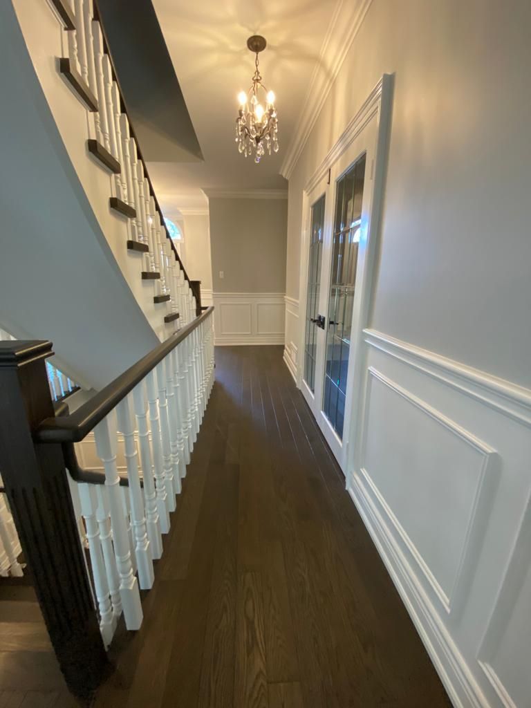 Hallway with dark wood floor, white wainscoting, a staircase, and a chandelier.