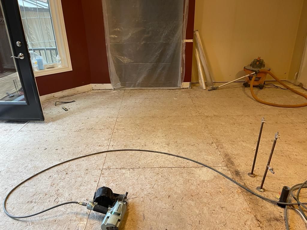 Room under construction, exposed subfloor, nail gun, air hose, and tools.