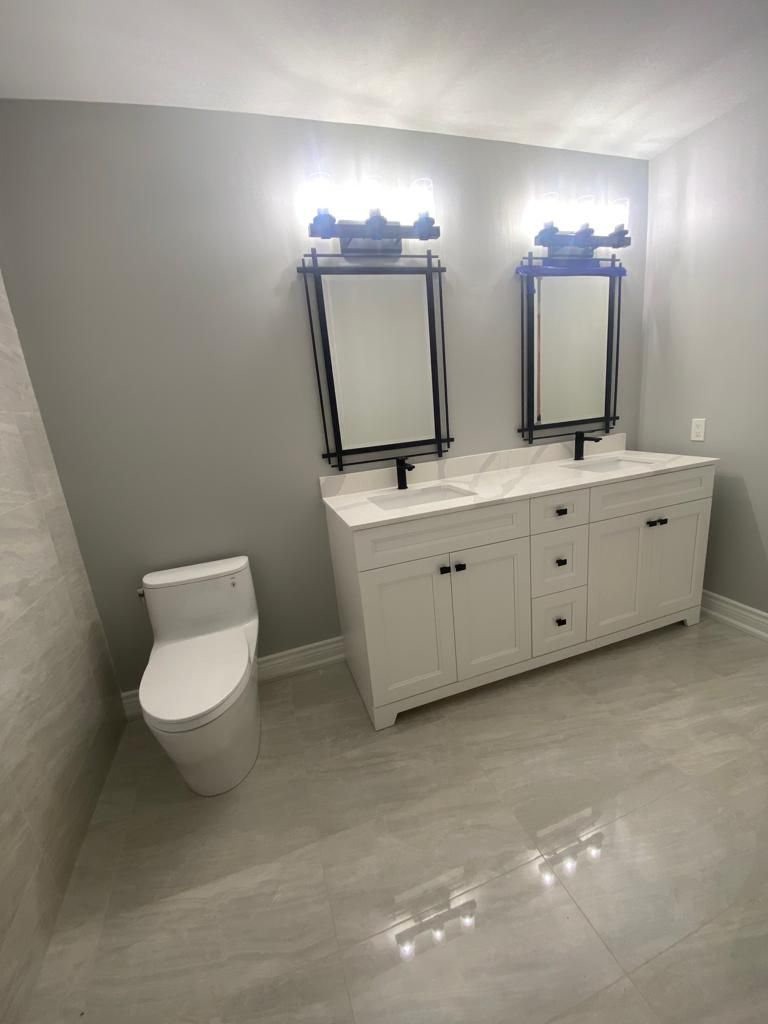 Modern bathroom with white double vanity, mirrors, and toilet. Gray walls and flooring.