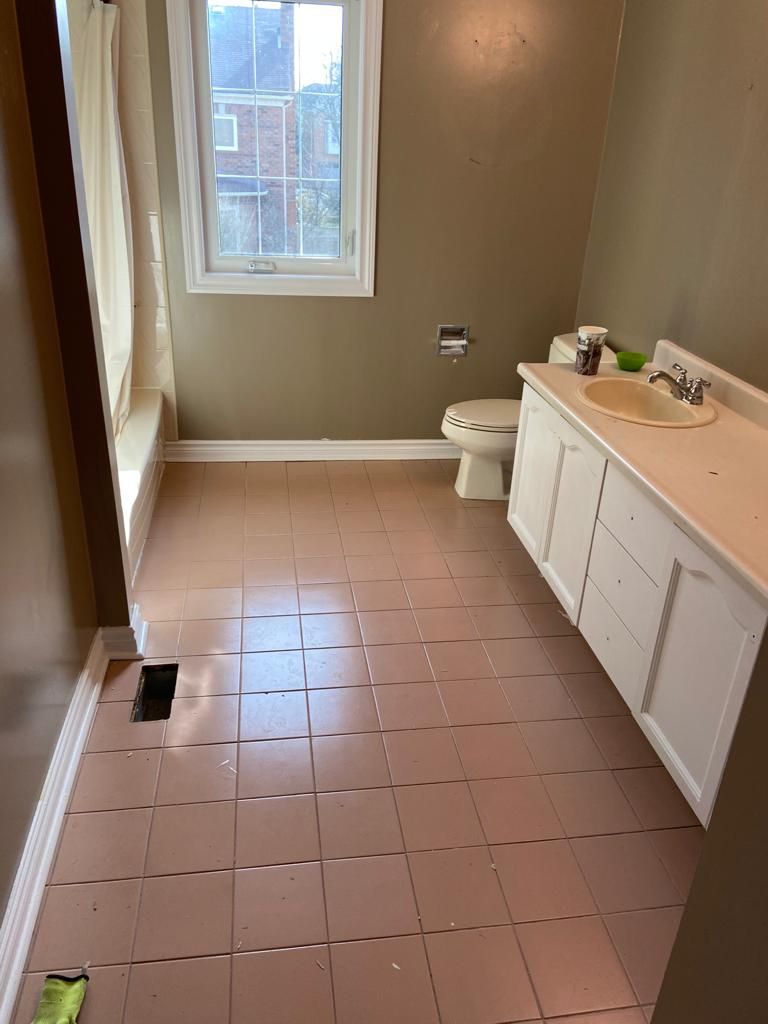 Bathroom with pink tiled floor, white vanity and toilet, and a window with natural light.