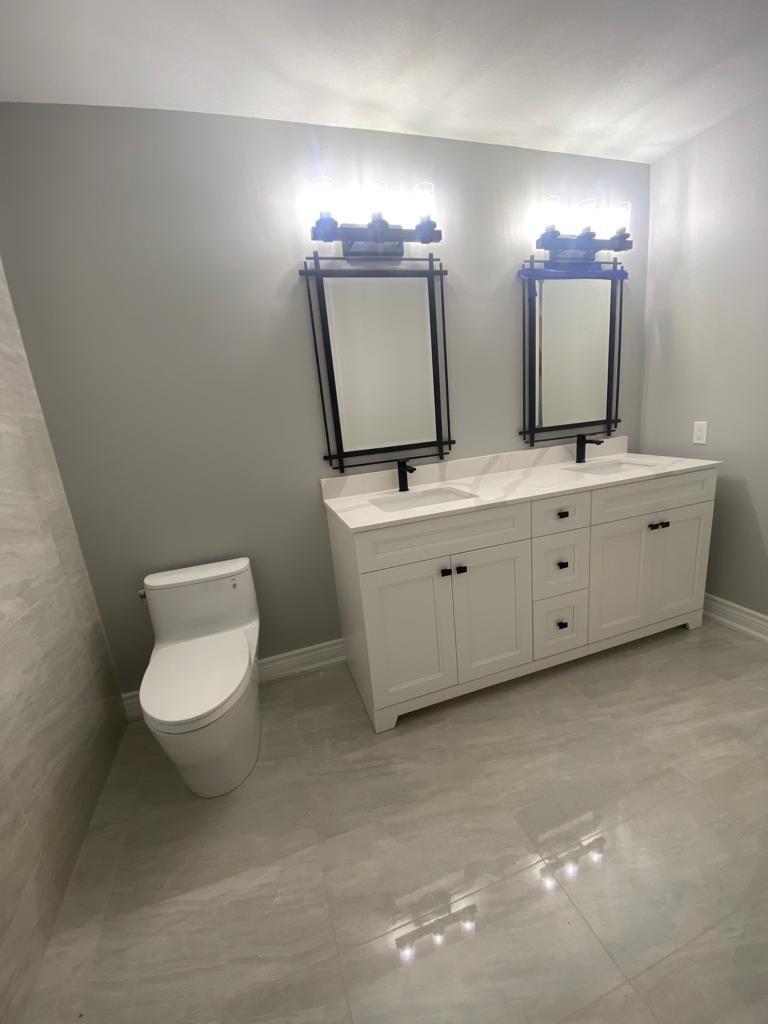 Modern bathroom with white double vanity, mirrors, toilet, and gray walls and floor.