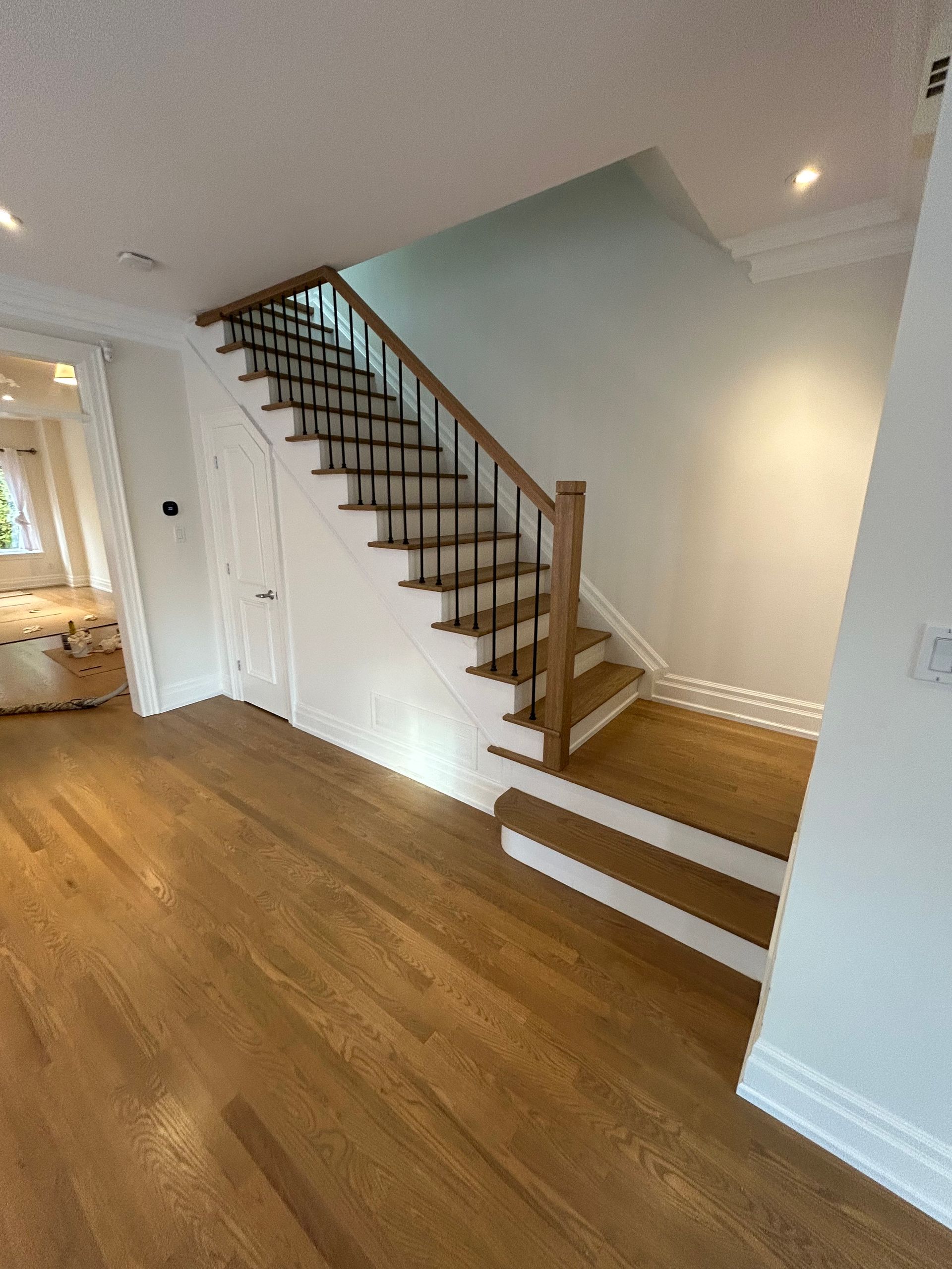 Wooden staircase with black railings, hardwood floors, and white walls.