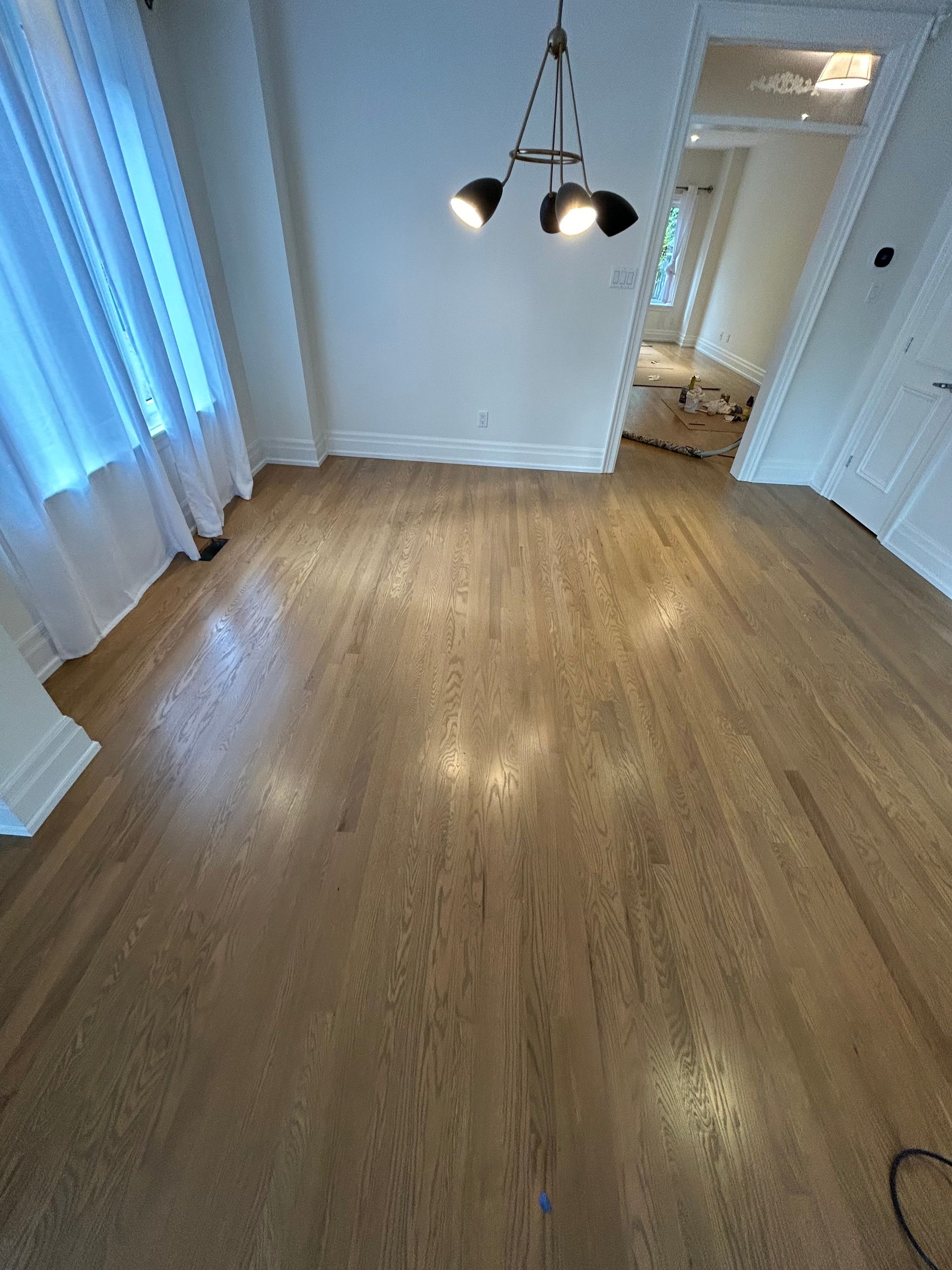 Hardwood floor in a room, with a modern light fixture and a sheer white curtain.