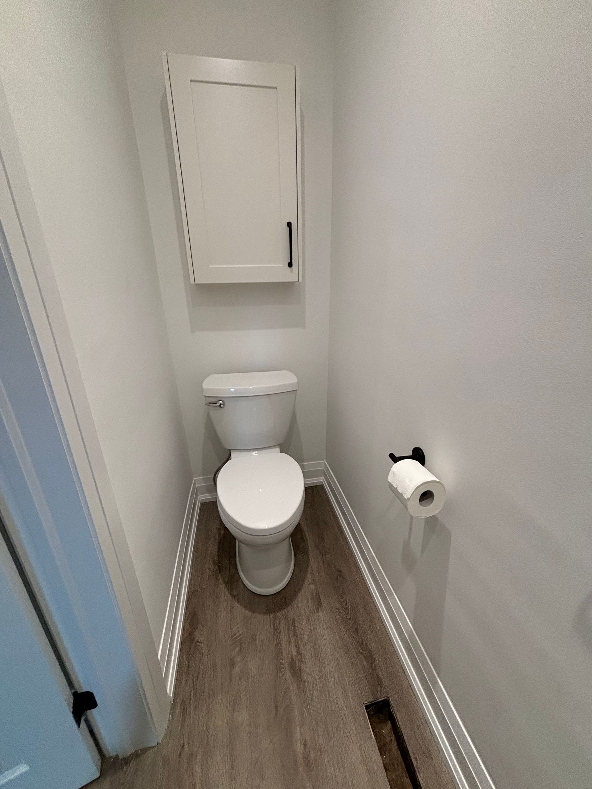 Small bathroom with toilet, storage cabinet, and roll of toilet paper on the wall.