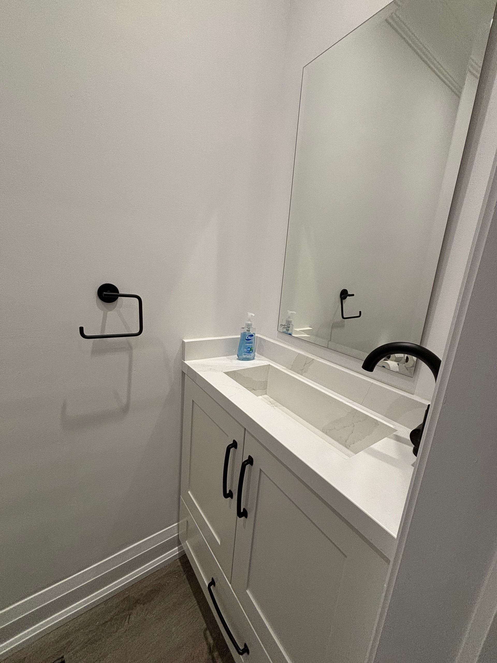White bathroom vanity with black hardware, mirror, and toilet paper holder.