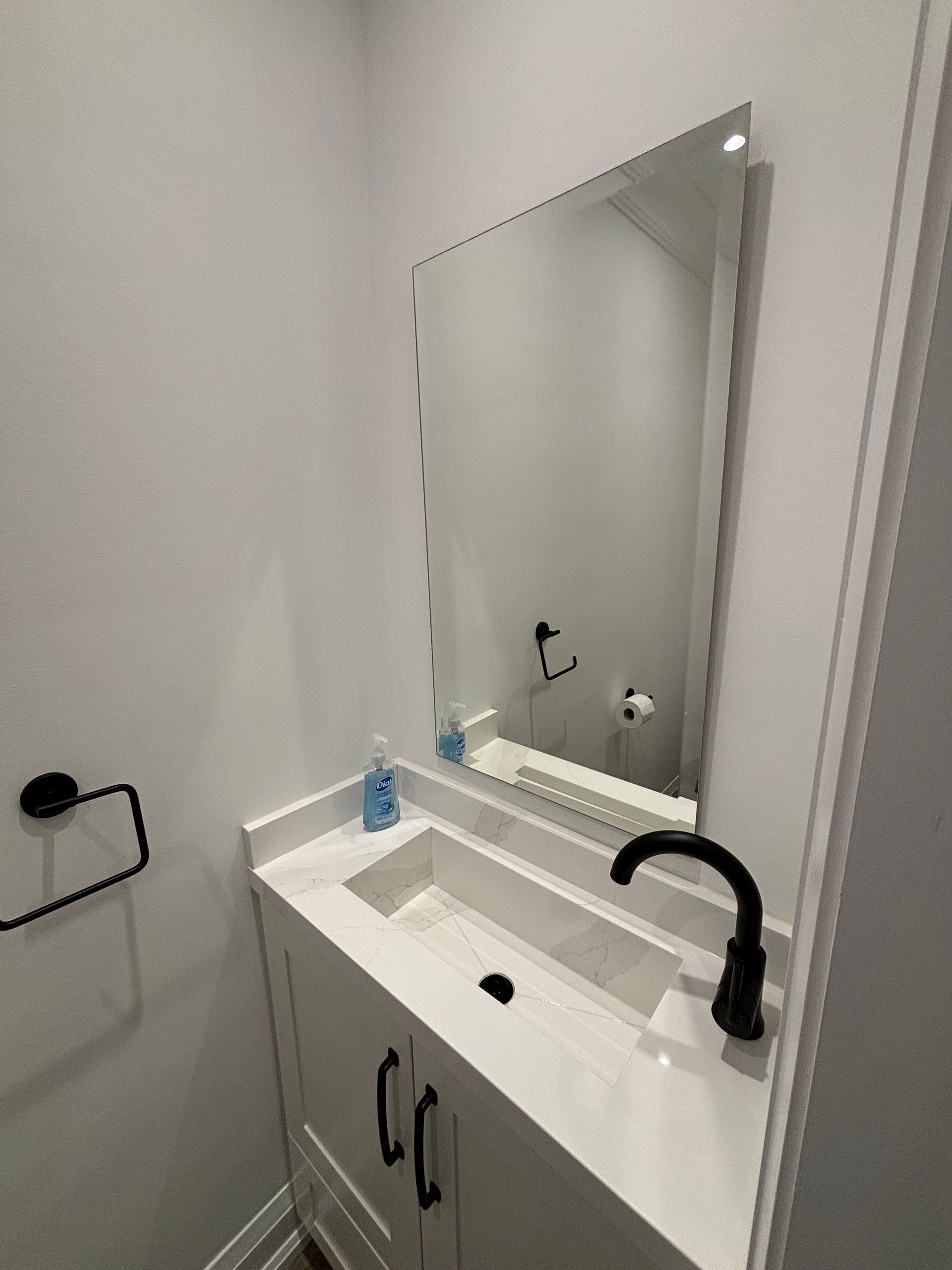 Small bathroom with white vanity, black faucet, and rectangular mirror.