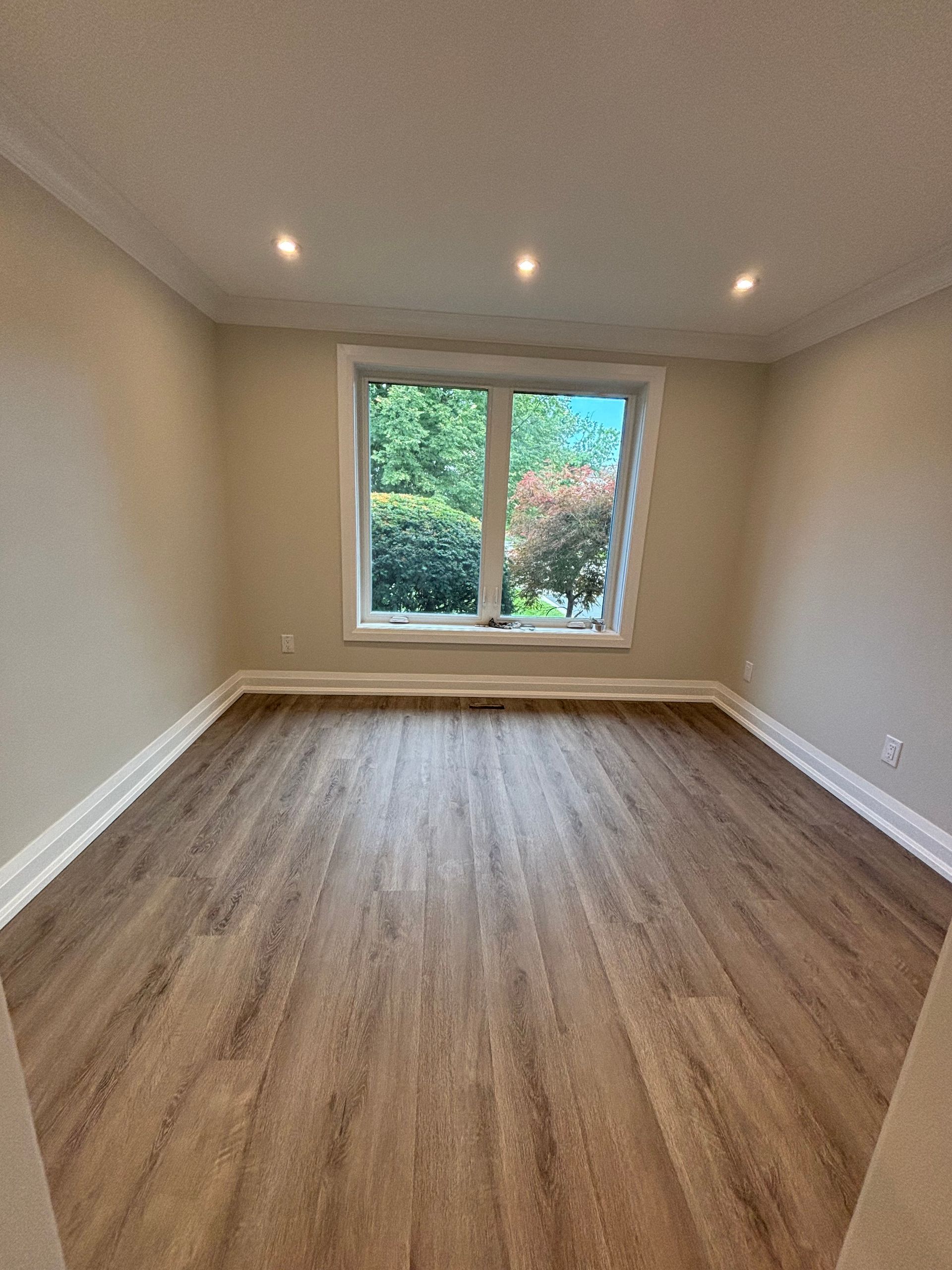 Empty room with hardwood floors, a window, and recessed ceiling lights.