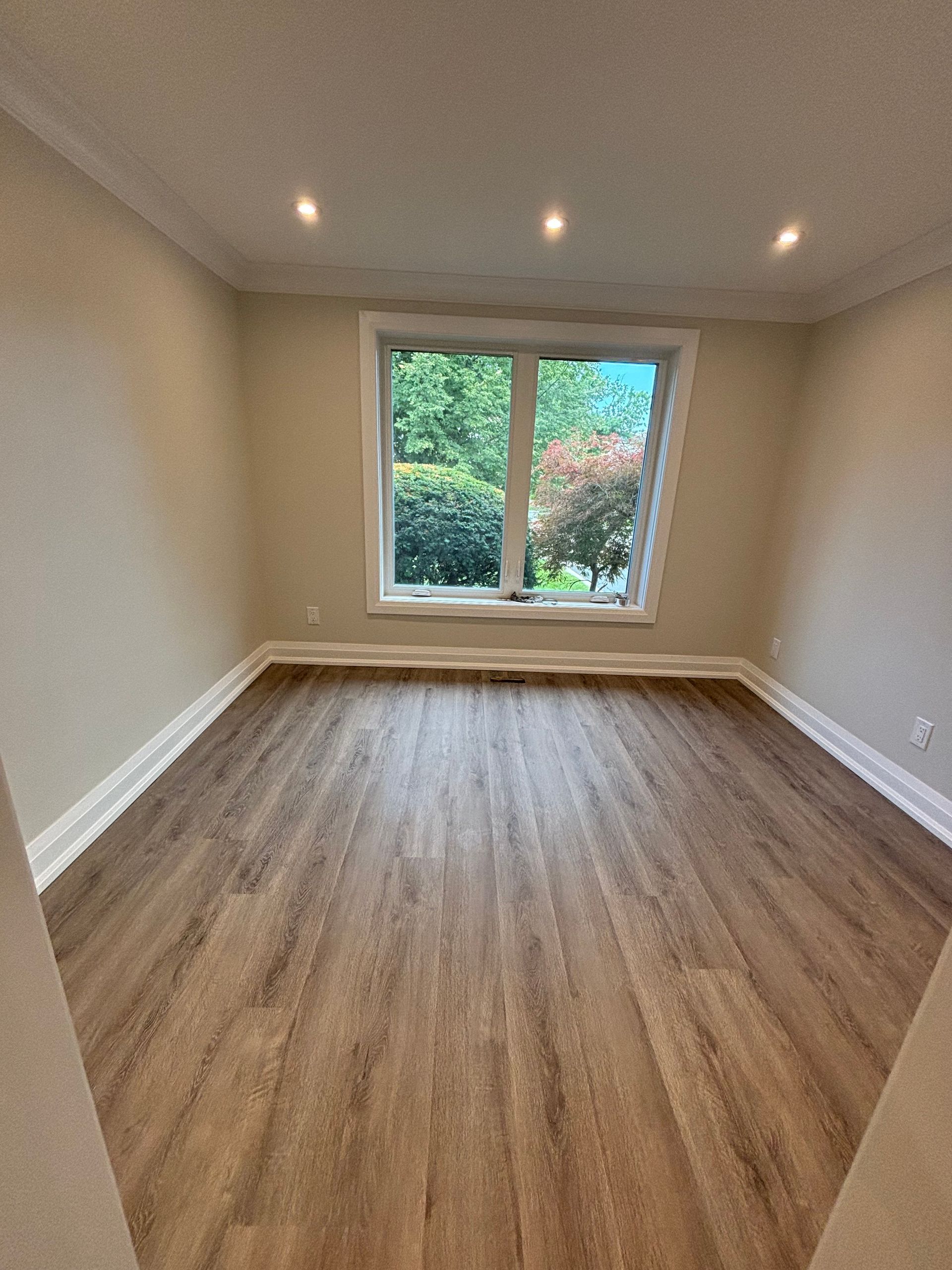Empty room with hardwood floors, a window, and recessed ceiling lights. Light beige walls.