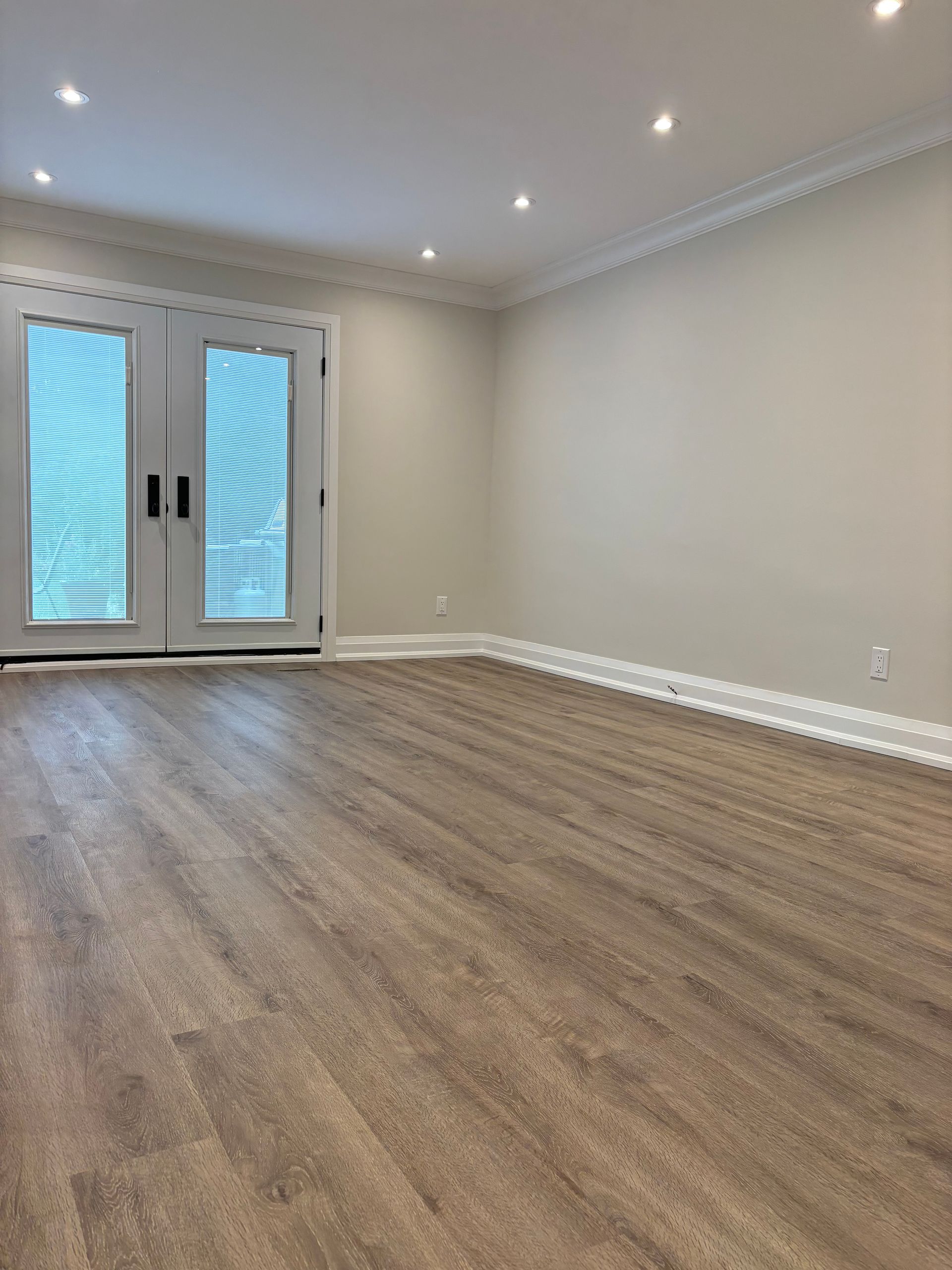 Empty room with French doors, beige walls, brown flooring, and white trim.