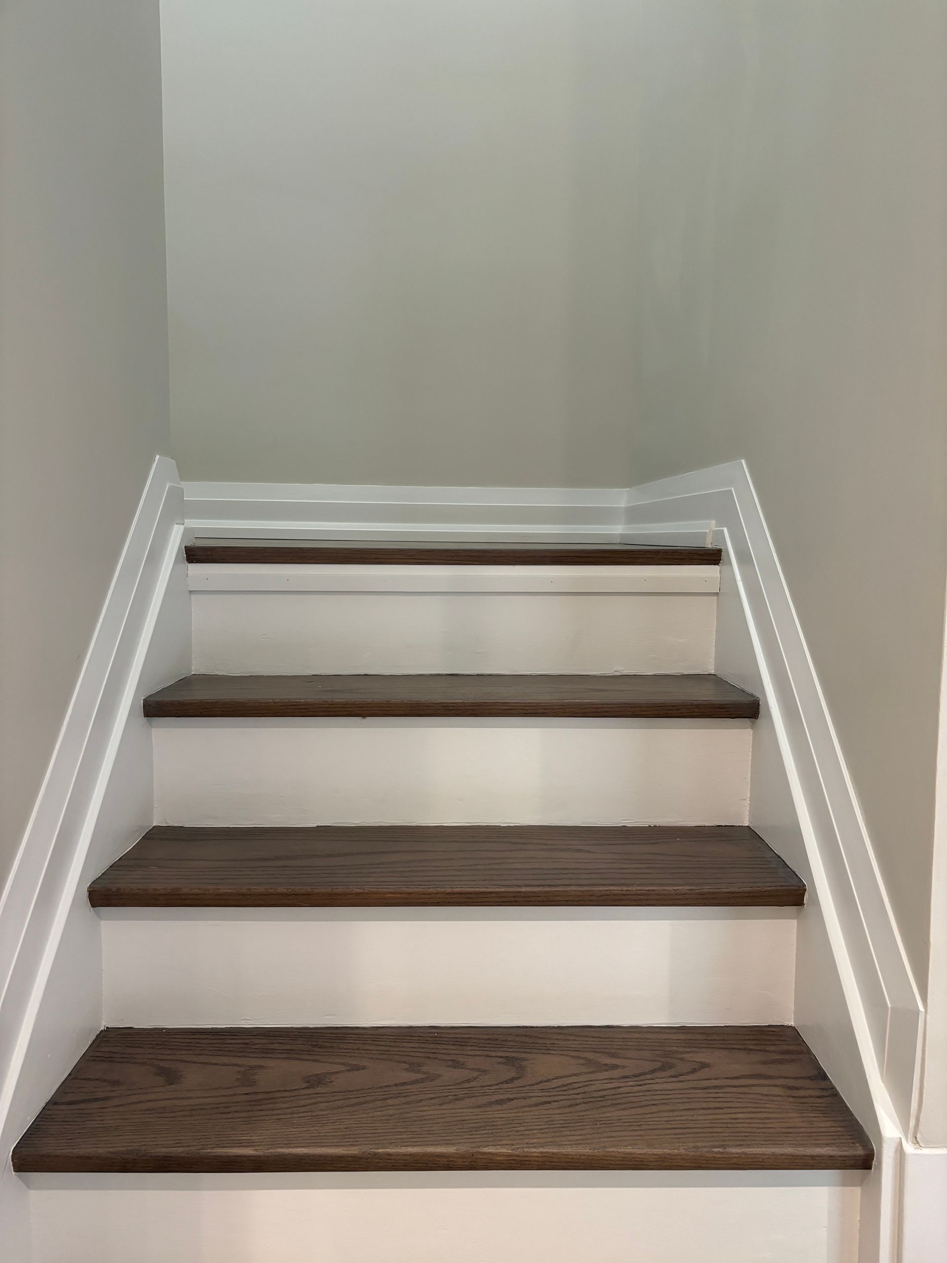 Wooden stair treads with white risers and walls, leading upwards.