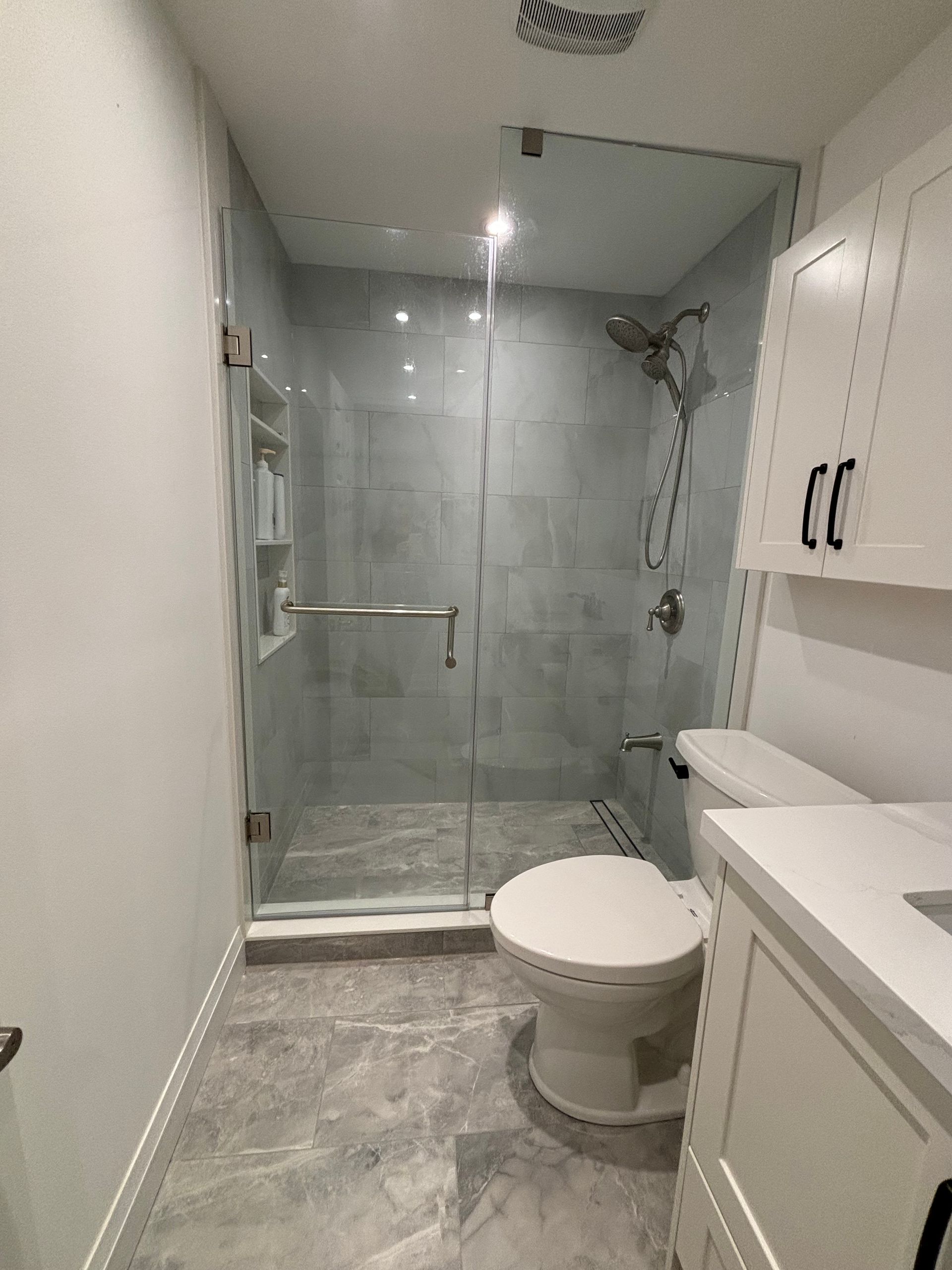 Bathroom with glass shower, white cabinetry, toilet, and gray tile flooring.