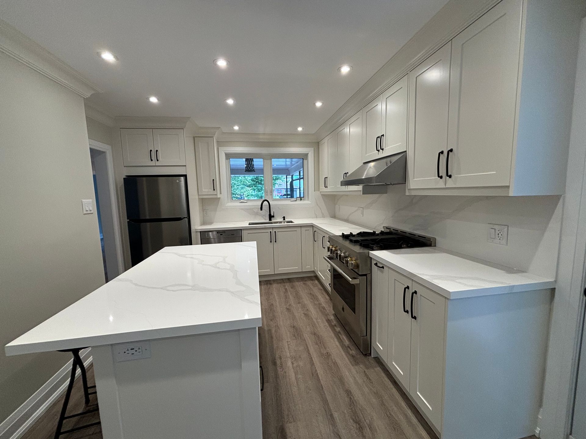 Newly renovated white kitchen with stainless steel appliances and an island.